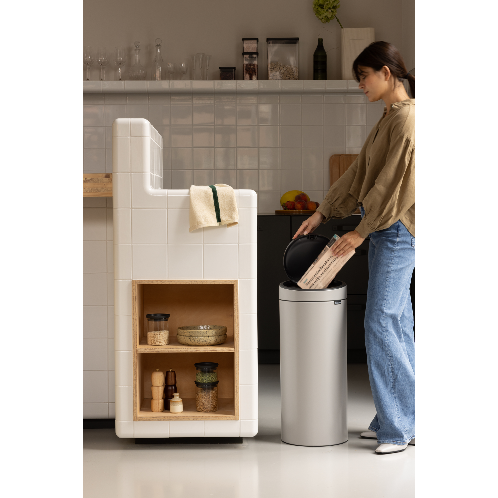 Een vrouw gooit een krant in een zilveren prullenbak in een moderne keuken.