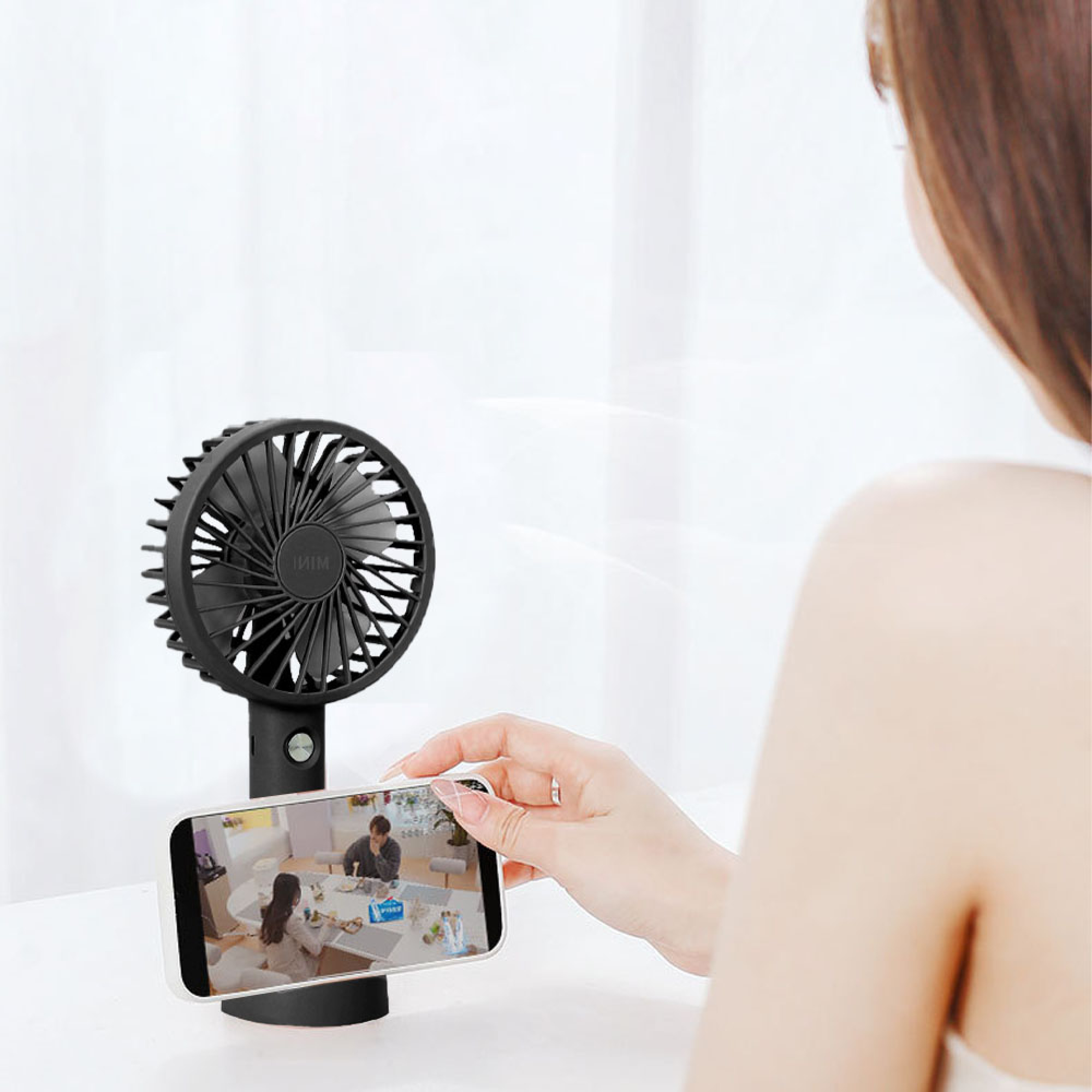 Ein schwarzer Mini-Ventilator steht neben einem Handy, das ein Paar an einem Tisch zeigt.