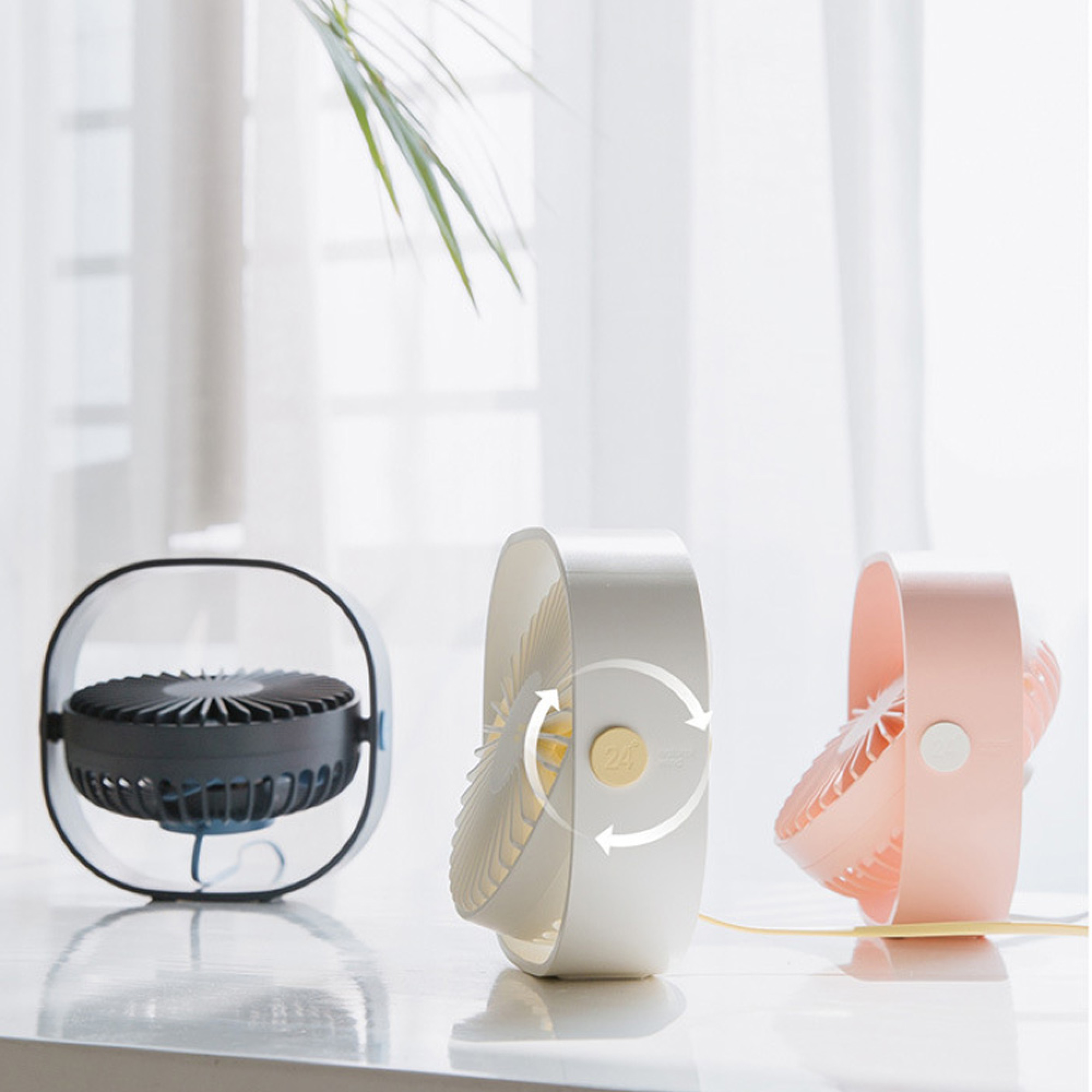 Drei kleine Ventilatoren auf einer Tischplatte vor einem hellen Fenster.