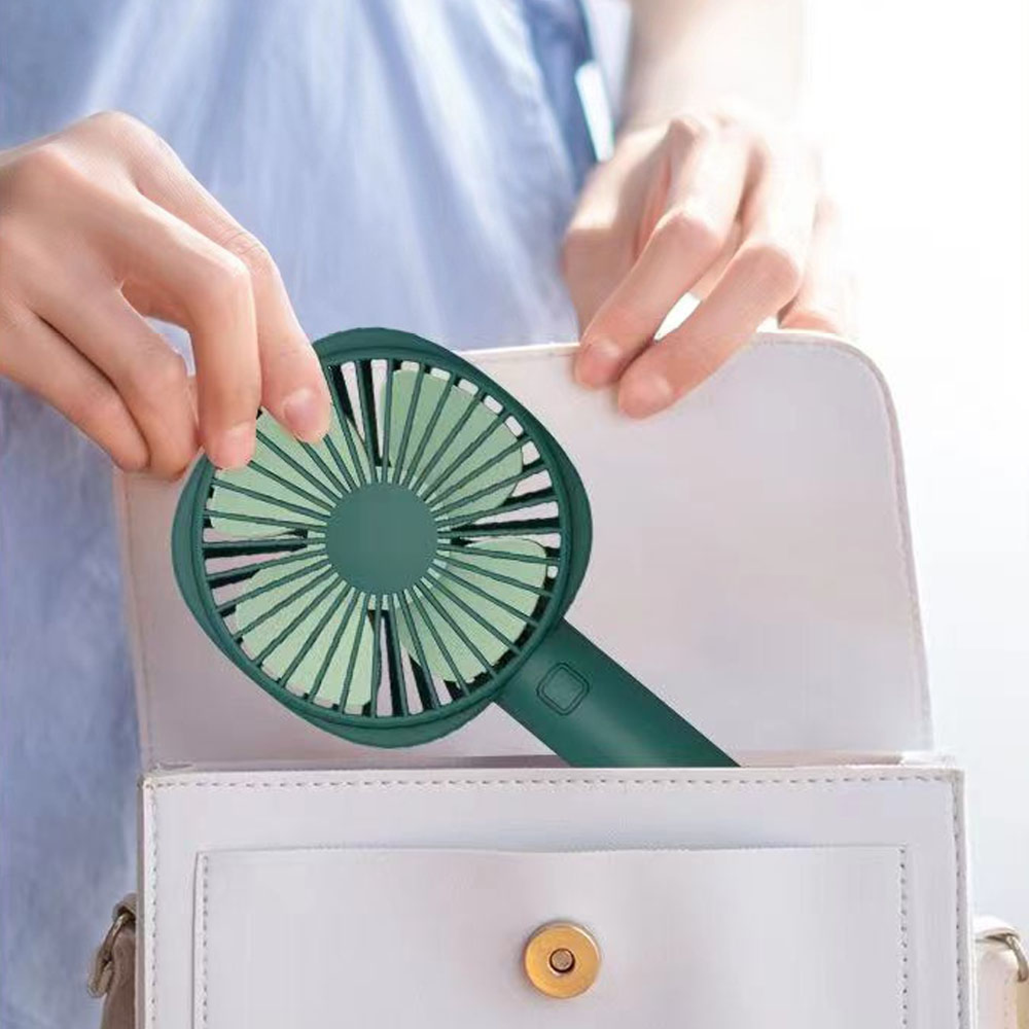Eine grüne Handventilator wird in eine weiße Tasche gelegt.