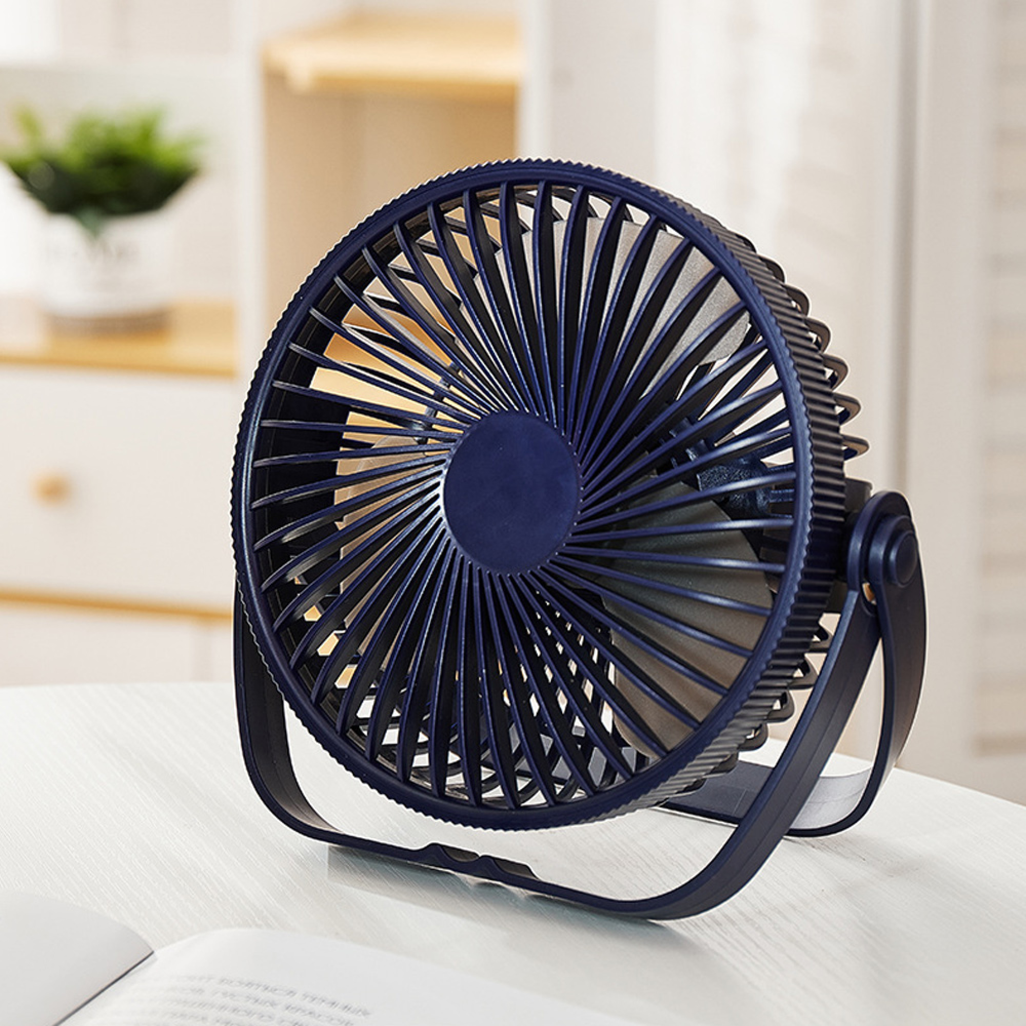 Ein dunkler Ventilator steht auf einem Tisch mit einem Buch davor.