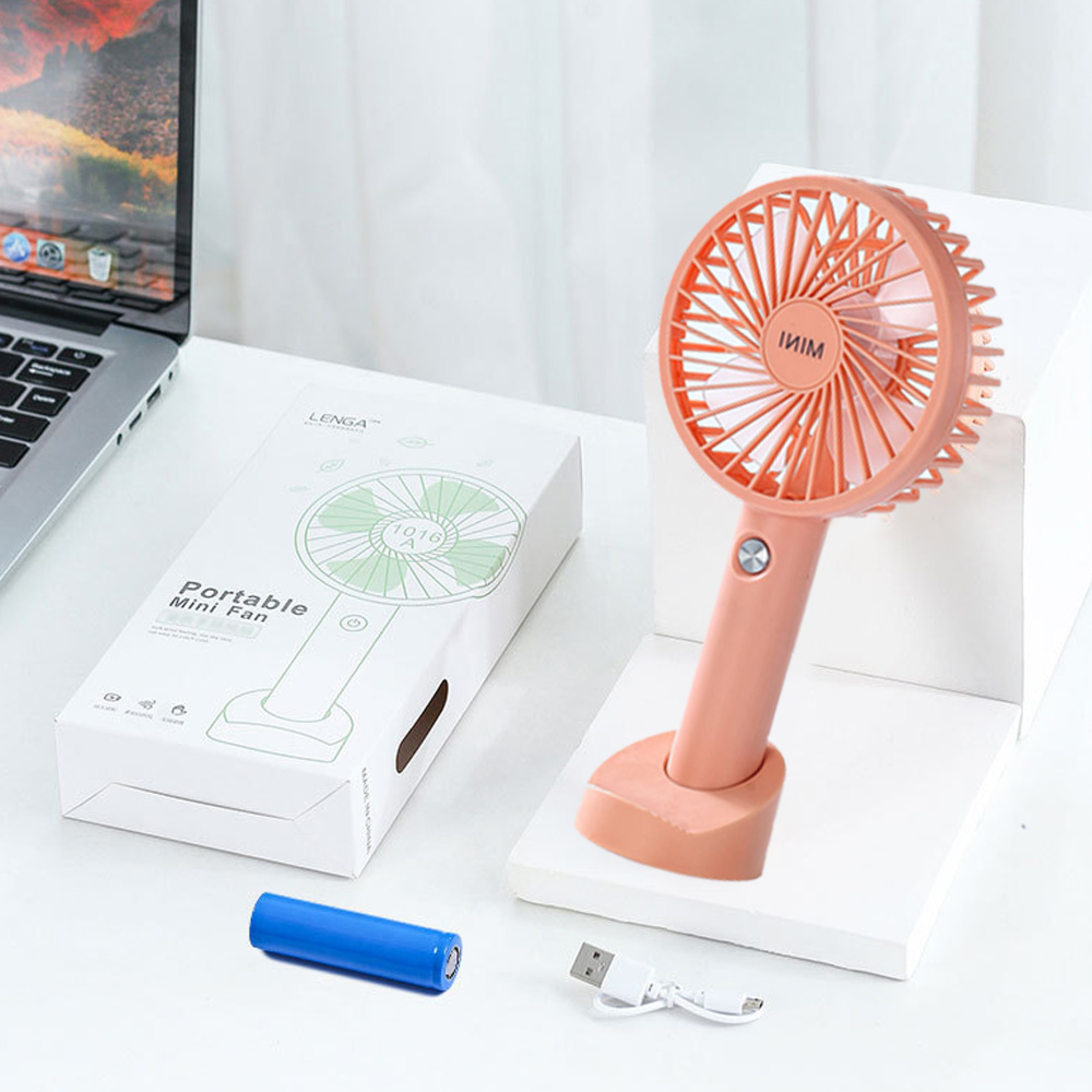 Ein rosafarbener Mini-Ventilator steht neben einer Verpackung und einem Laptop.