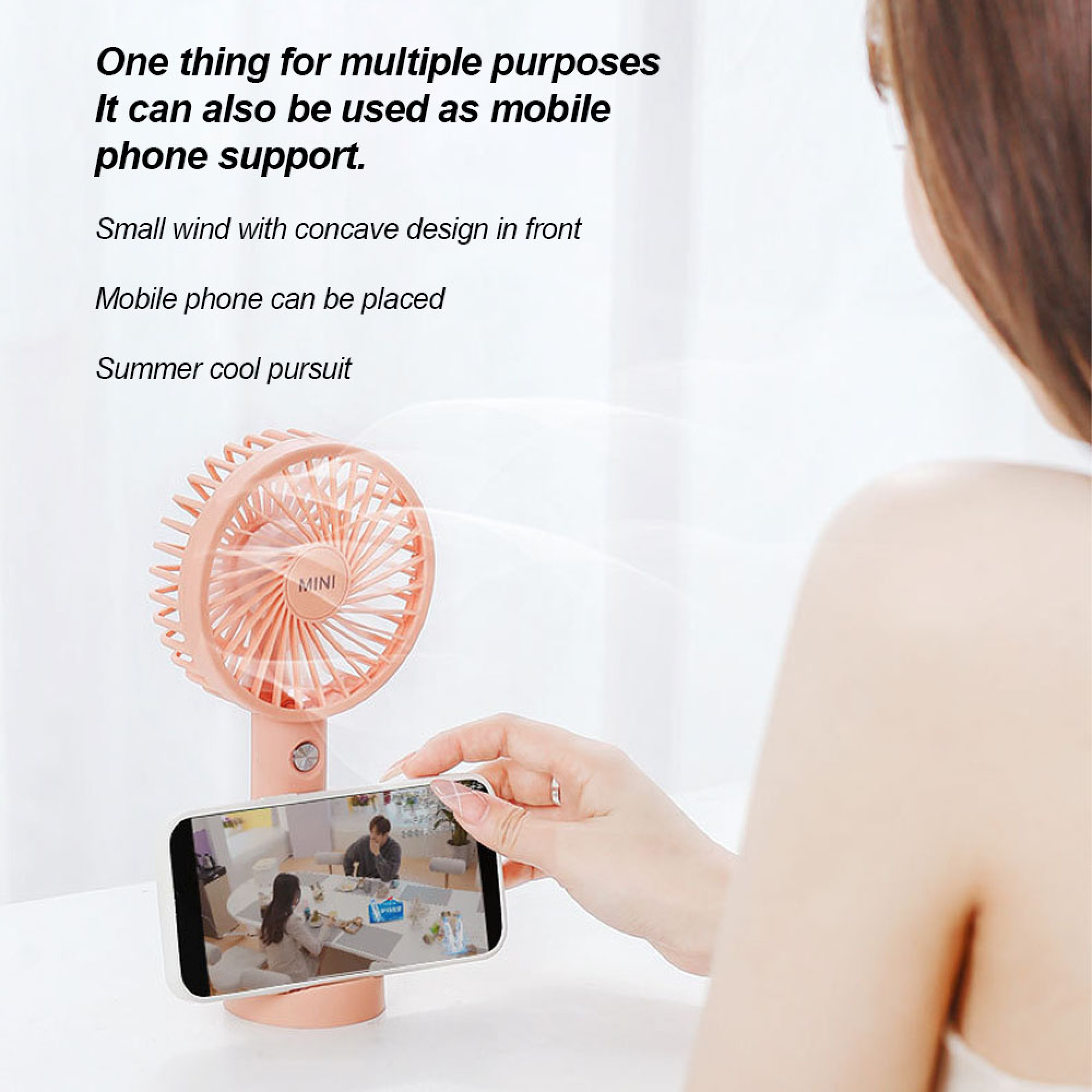 Ein pinker Mini-Ventilator steht neben einem Handy, das eine Person hält und ein Video zeigt.