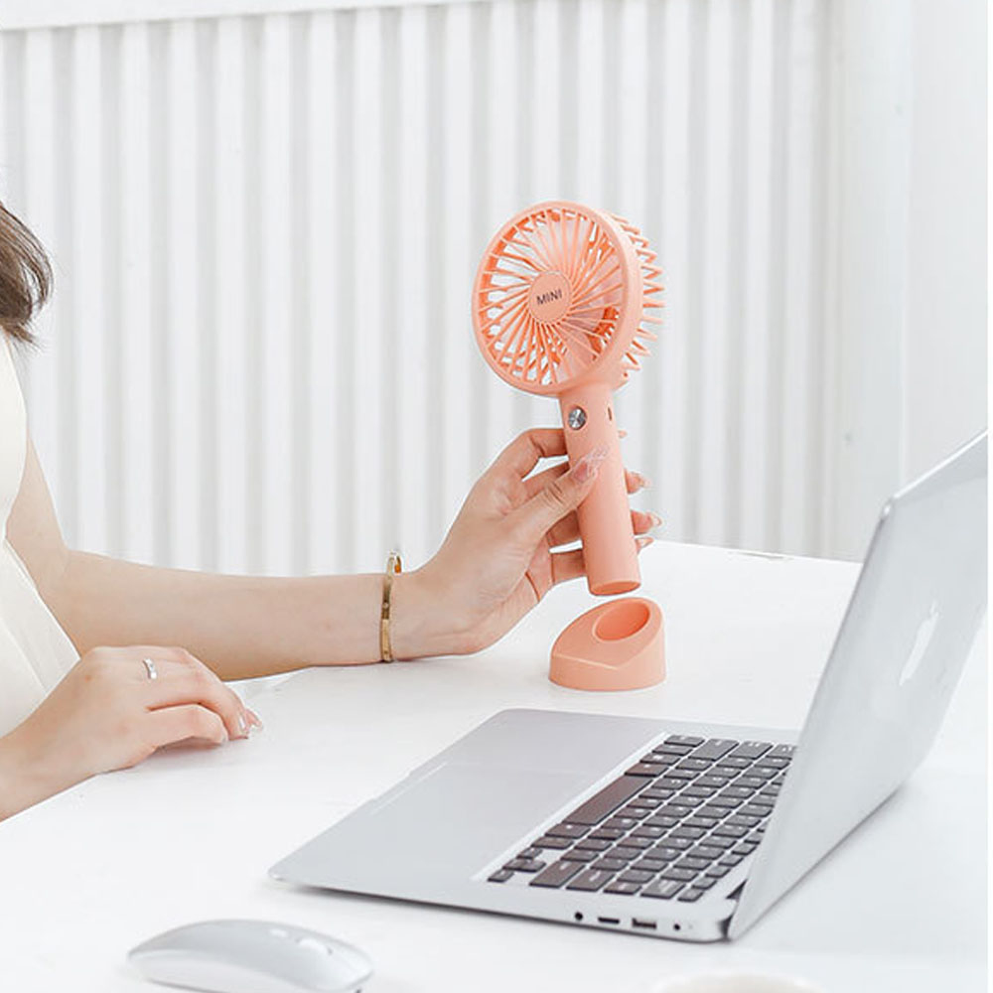 Eine Hand hält einen rosa Mini-Ventilator neben einem Laptop und einer Maus.