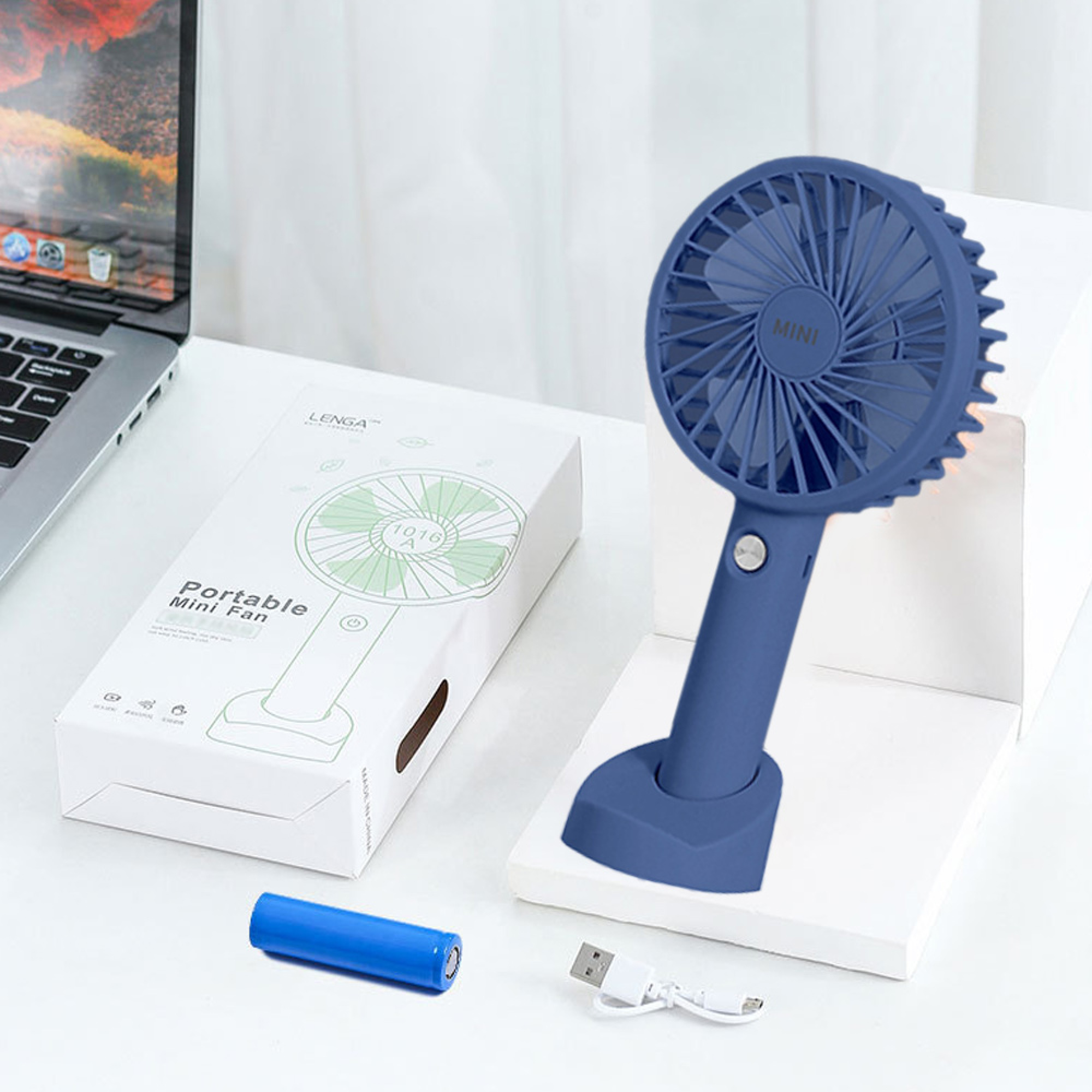 Ein blauer Mini-Ventilator mit Lade-Akku, USB-Kabel und Laptop auf weißem Tisch.