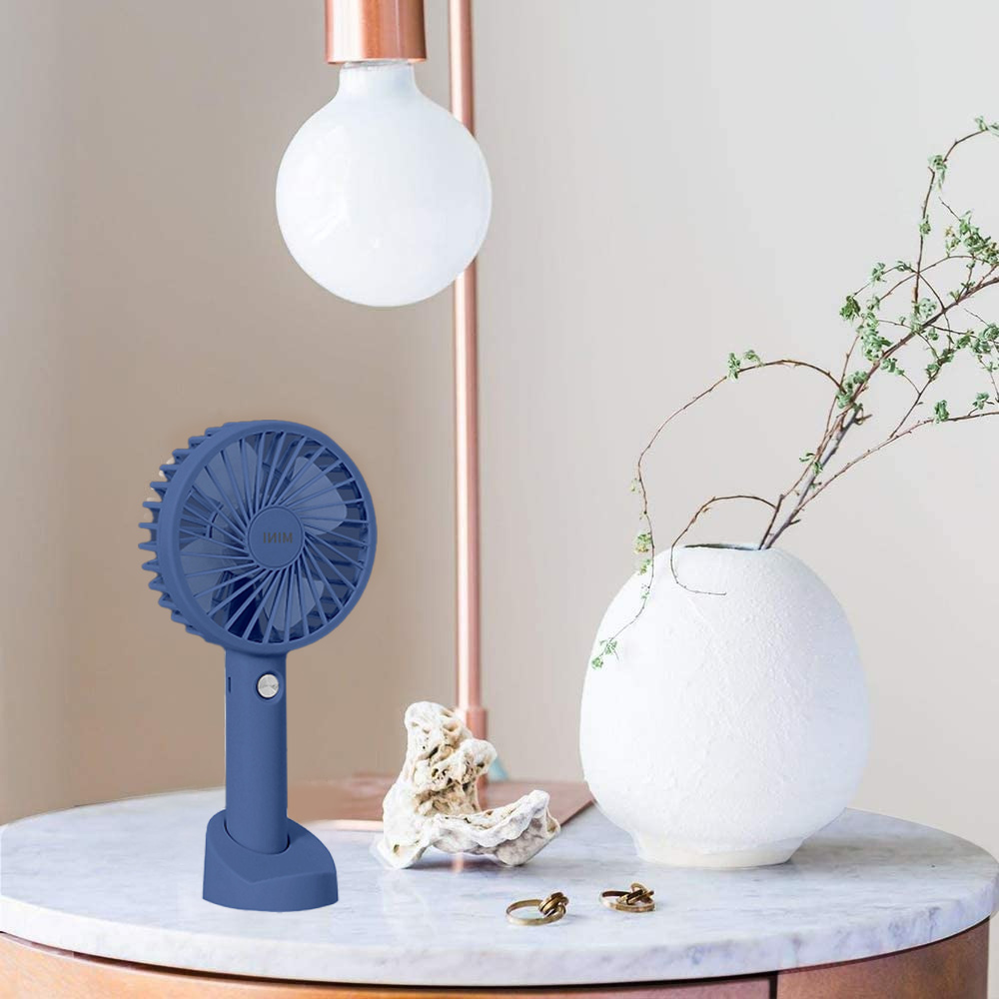 Ein blauer Ventilator steht auf einem Marmortisch neben einer Vase mit Zweigen.