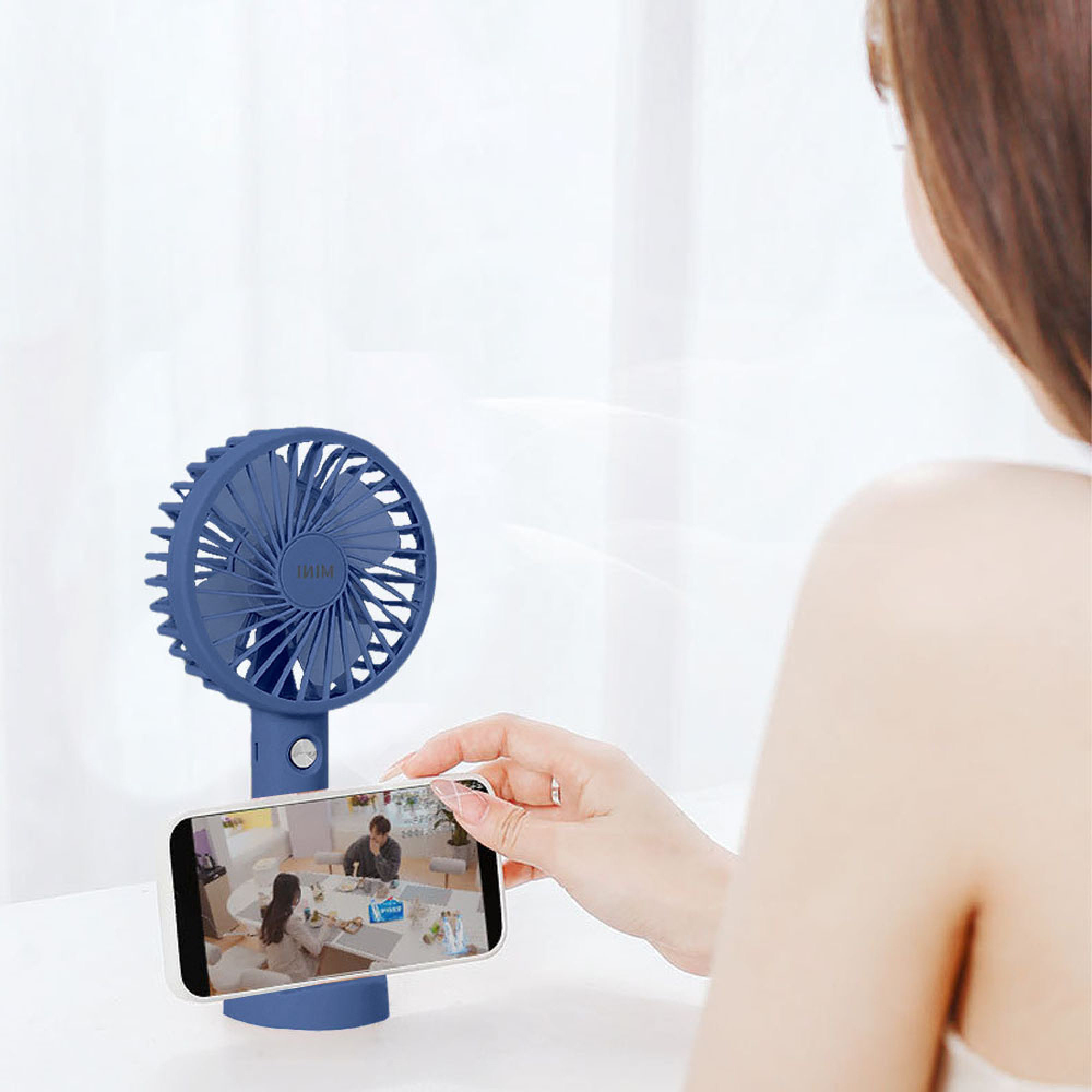 Eine Person hält ein Smartphone, das auf einem blauen Mini-Ventilator montiert ist.