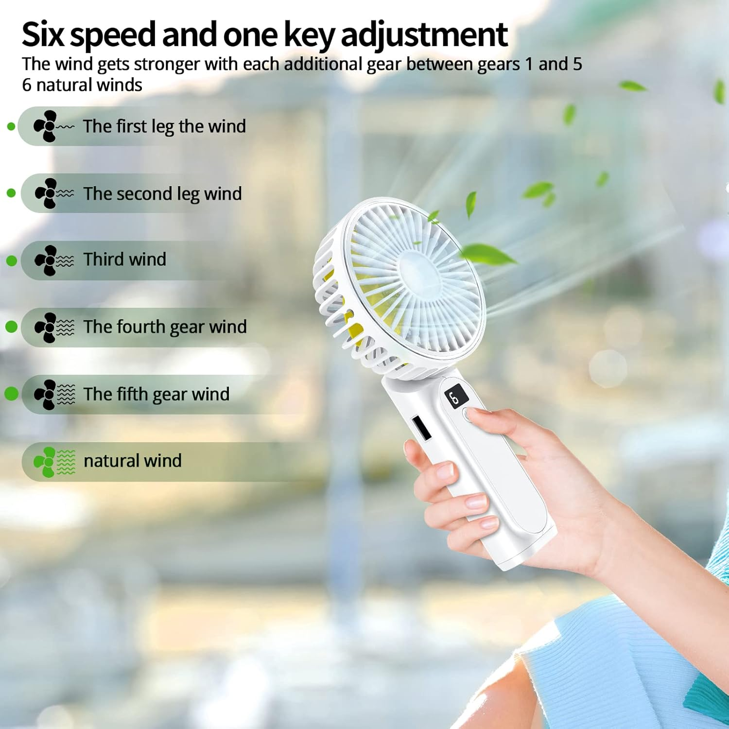 Ein weißer tragbarer Ventilator mit 6 Geschwindigkeitsstufen wird von einer Hand gehalten. Grüne Blätter schweben in der Luft.