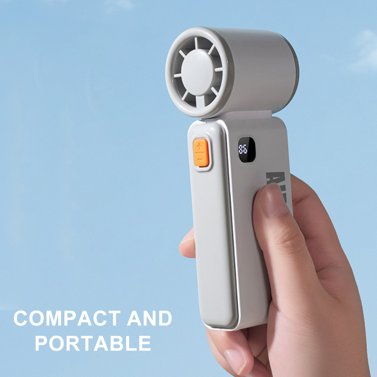 Graues Handventilator mit orangefarbenem Knopf wird in der Hand gehalten.