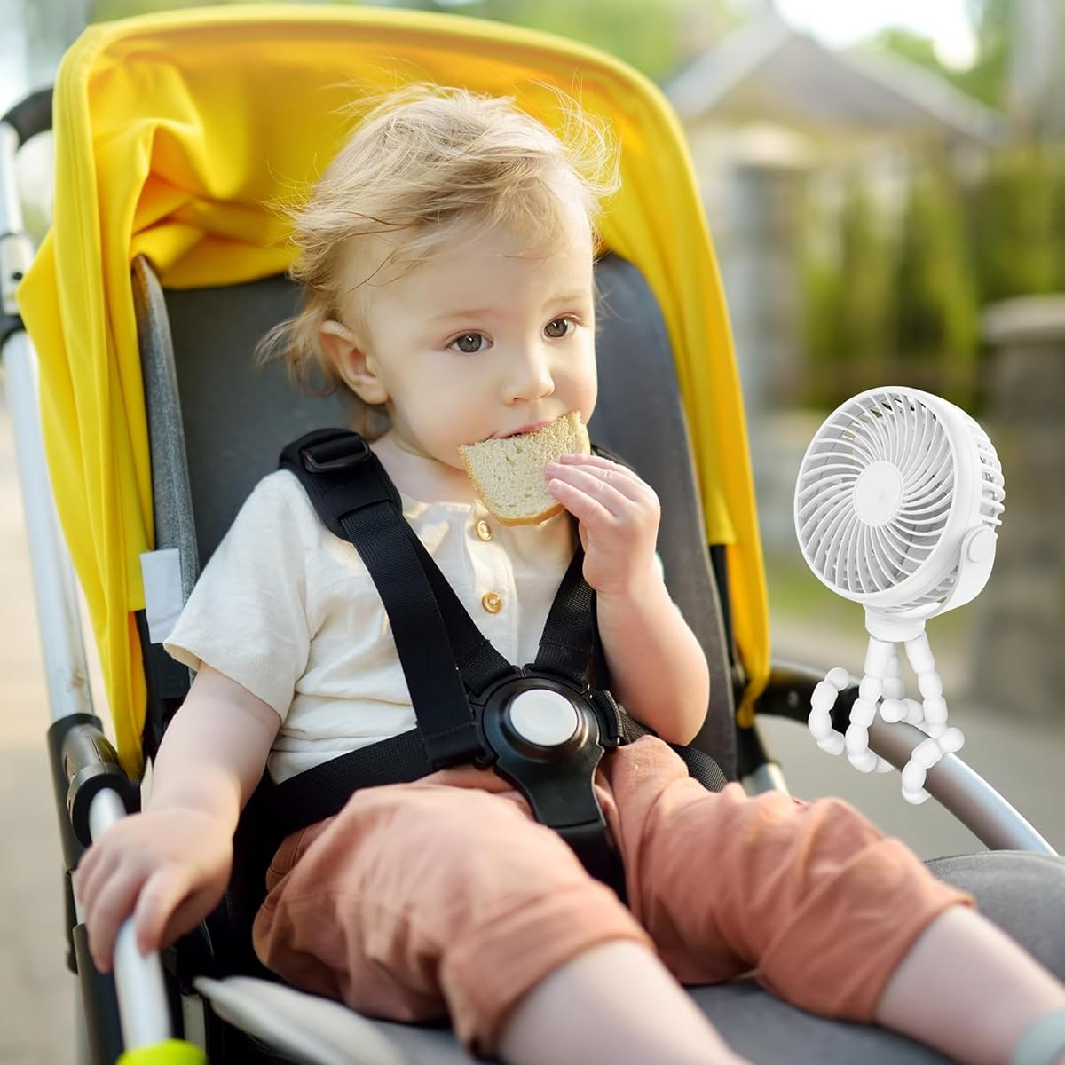 Ein Kleinkind isst Brot in einem gelben Kinderwagen mit einem weißen Ventilator in der Nähe.