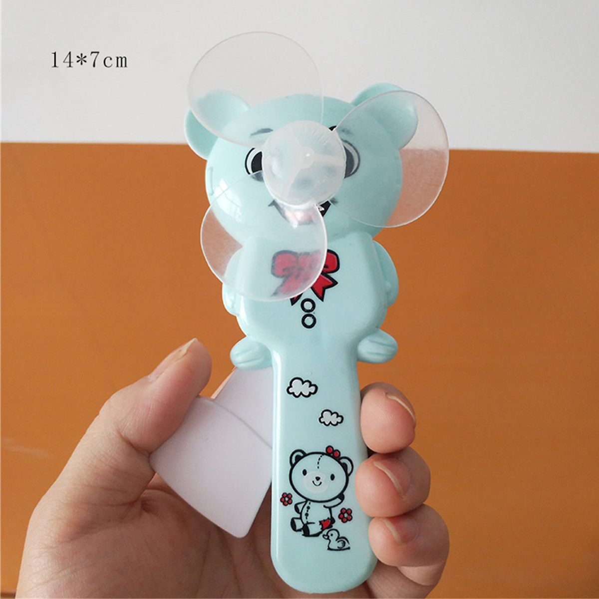Ein hellblauer Teddybär-Ventilator mit transparenten Flügeln wird in einer Hand gehalten.