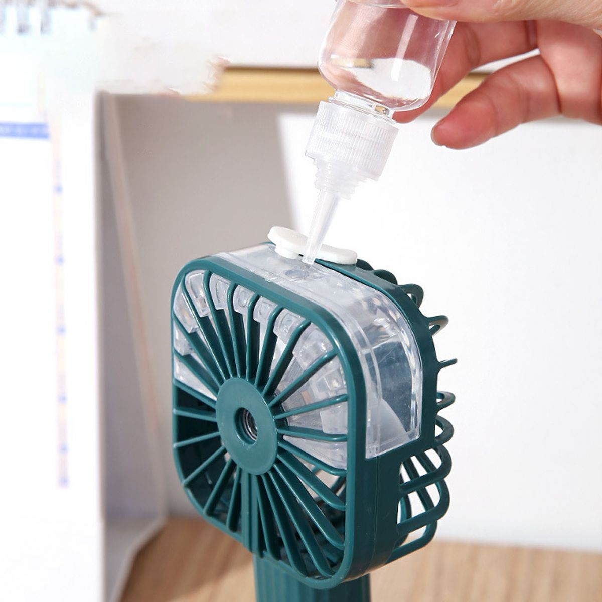 Eine Hand füllt eine kleine Flasche mit Flüssigkeit in einen kleinen grünen Ventilator.