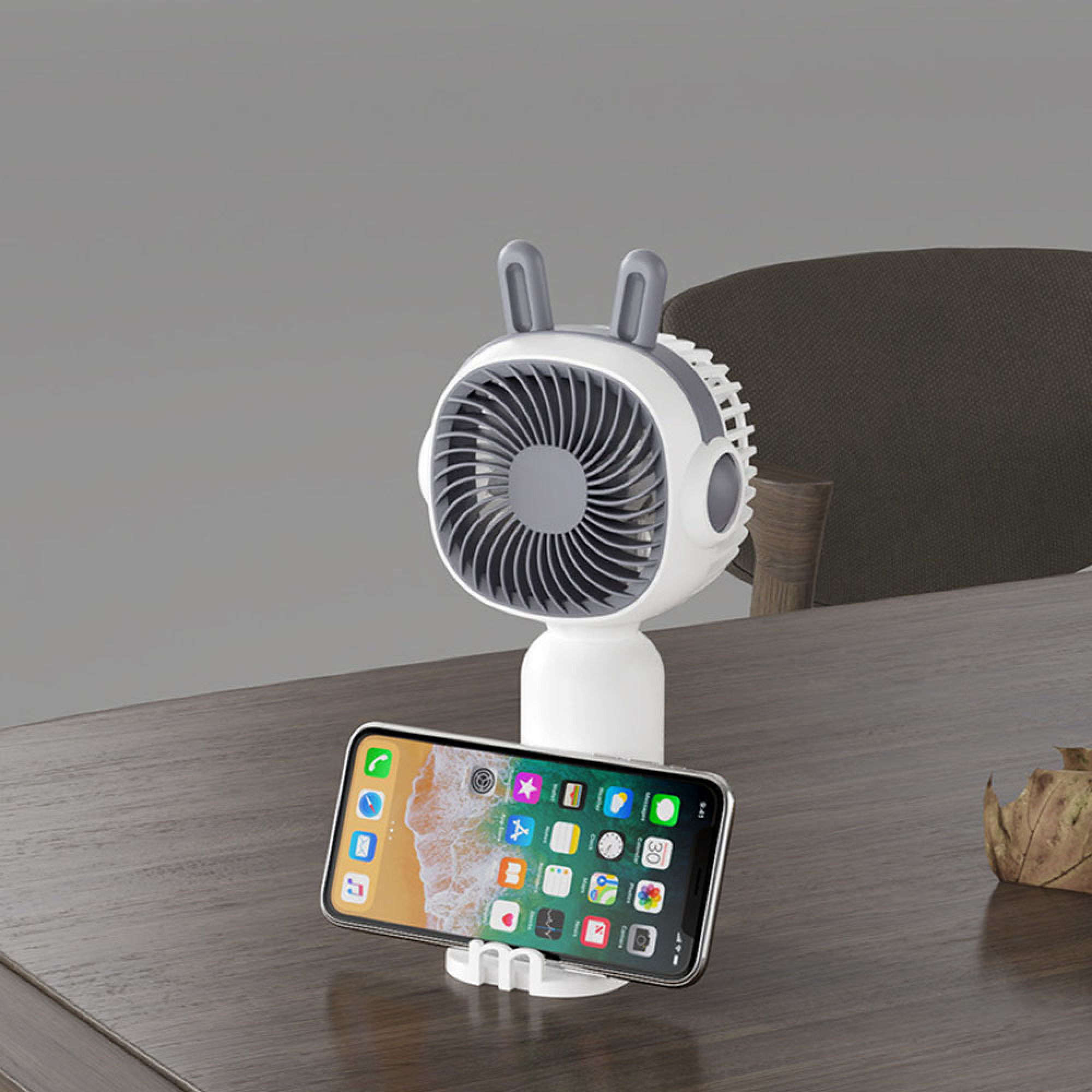 Ein weißer Ventilator mit grauen Hasenohren hält ein Smartphone auf einem Schreibtisch.