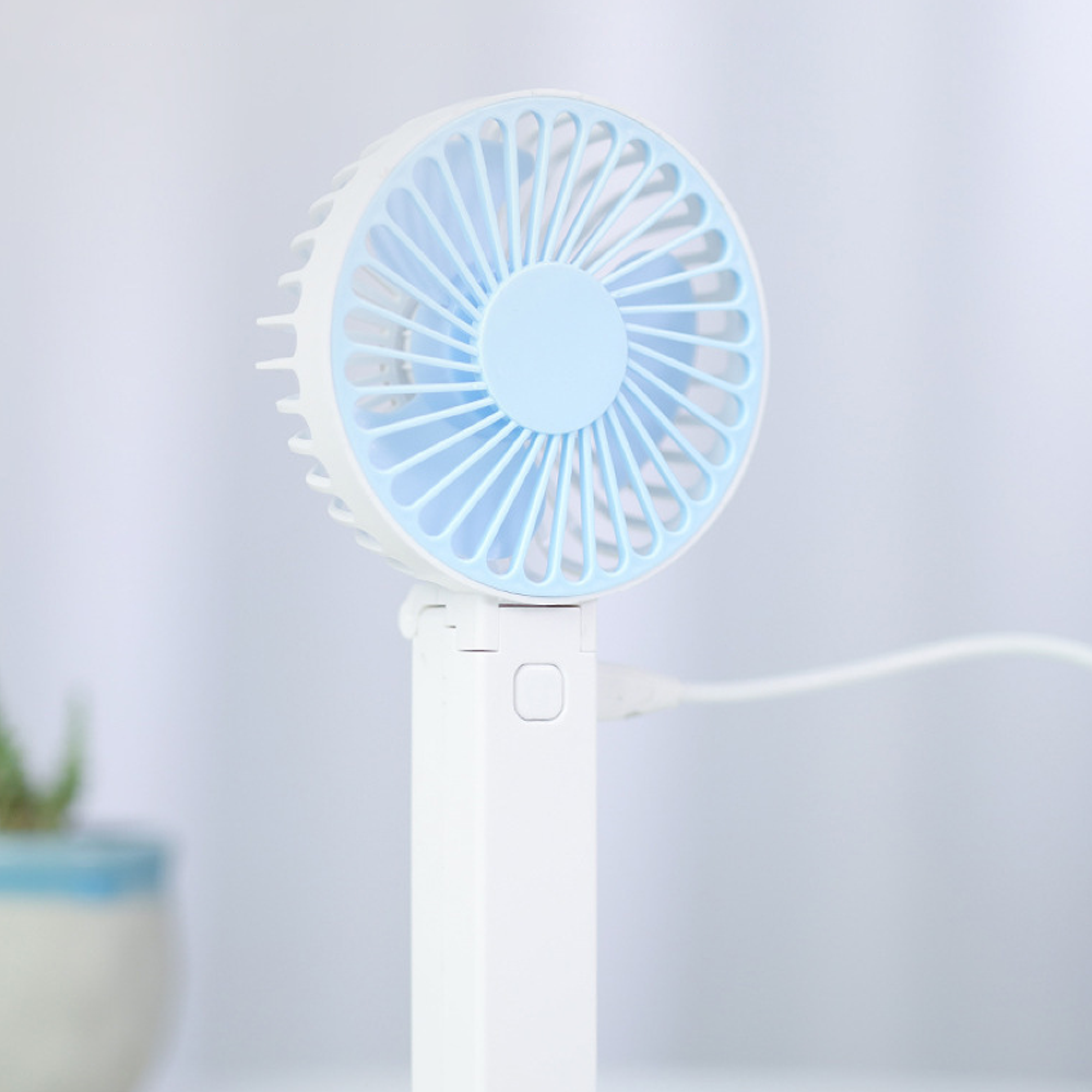 Ein kleiner weißer Ventilator mit blauem Rotorblatt, auf einem Tisch.