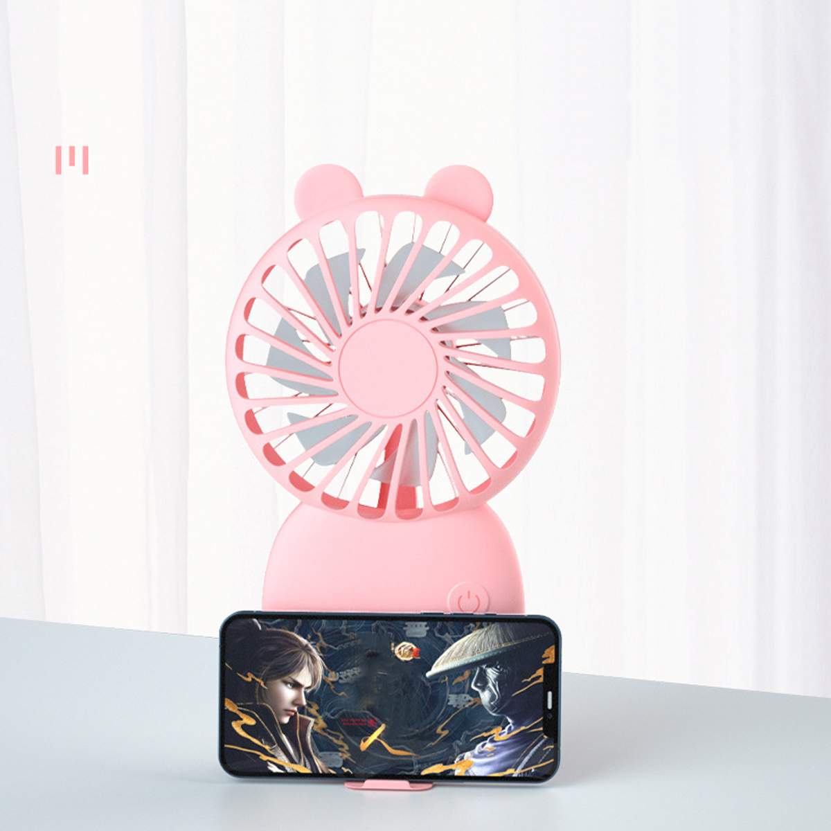 Ein rosafarbener Ventilator mit Bärenohren steht über einem Smartphone mit Spielbildschirm.