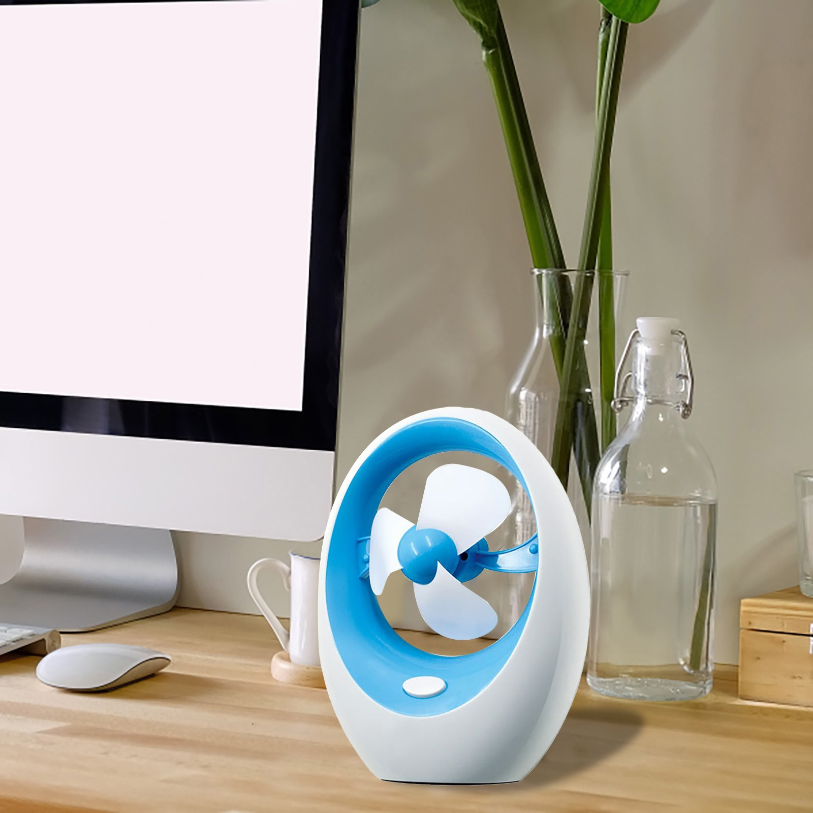 Ein blauer und weißer Ventilator steht auf einem Holzschreibtisch neben einem Computermonitor.