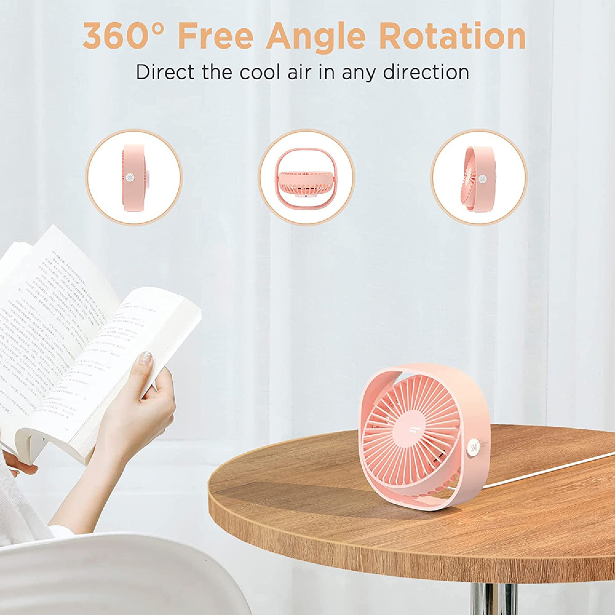 Ein kleiner rosa Ventilator auf einem Holztisch neben einem geöffneten Buch.