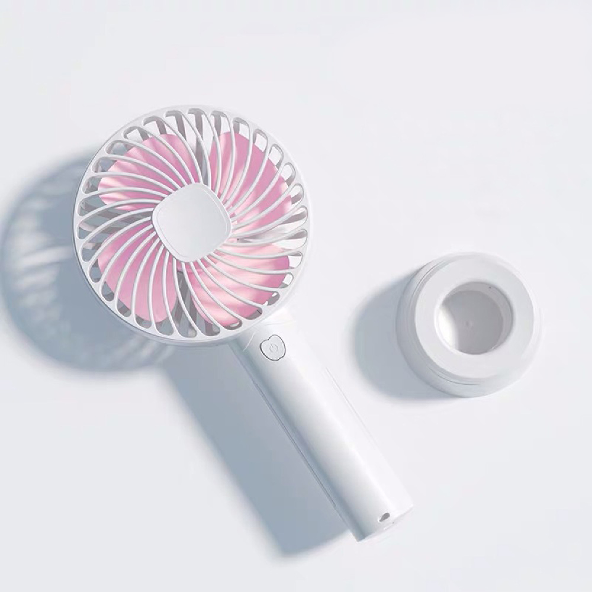Ein weißer Handventilator mit rosa Rotorblättern und ein Ständer auf weißem Hintergrund.