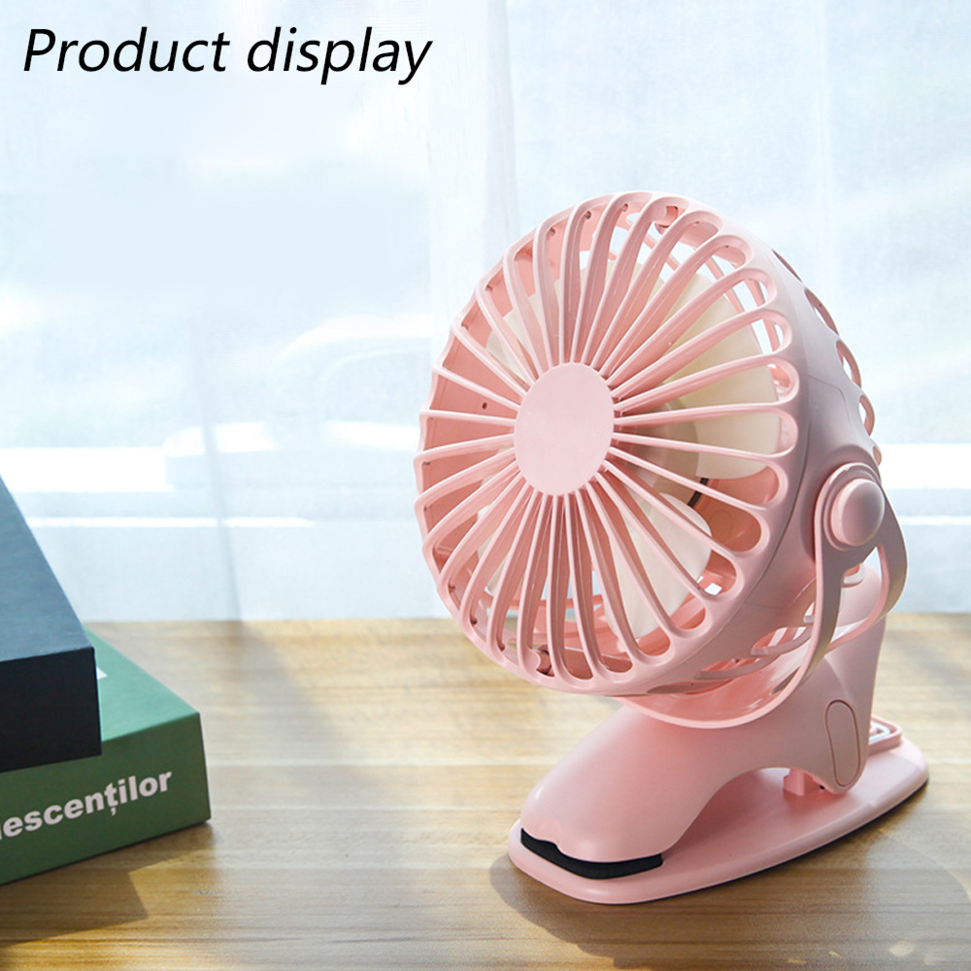 Ein rosafarbener Clip-Ventilator steht auf einem Holztisch neben Büchern.