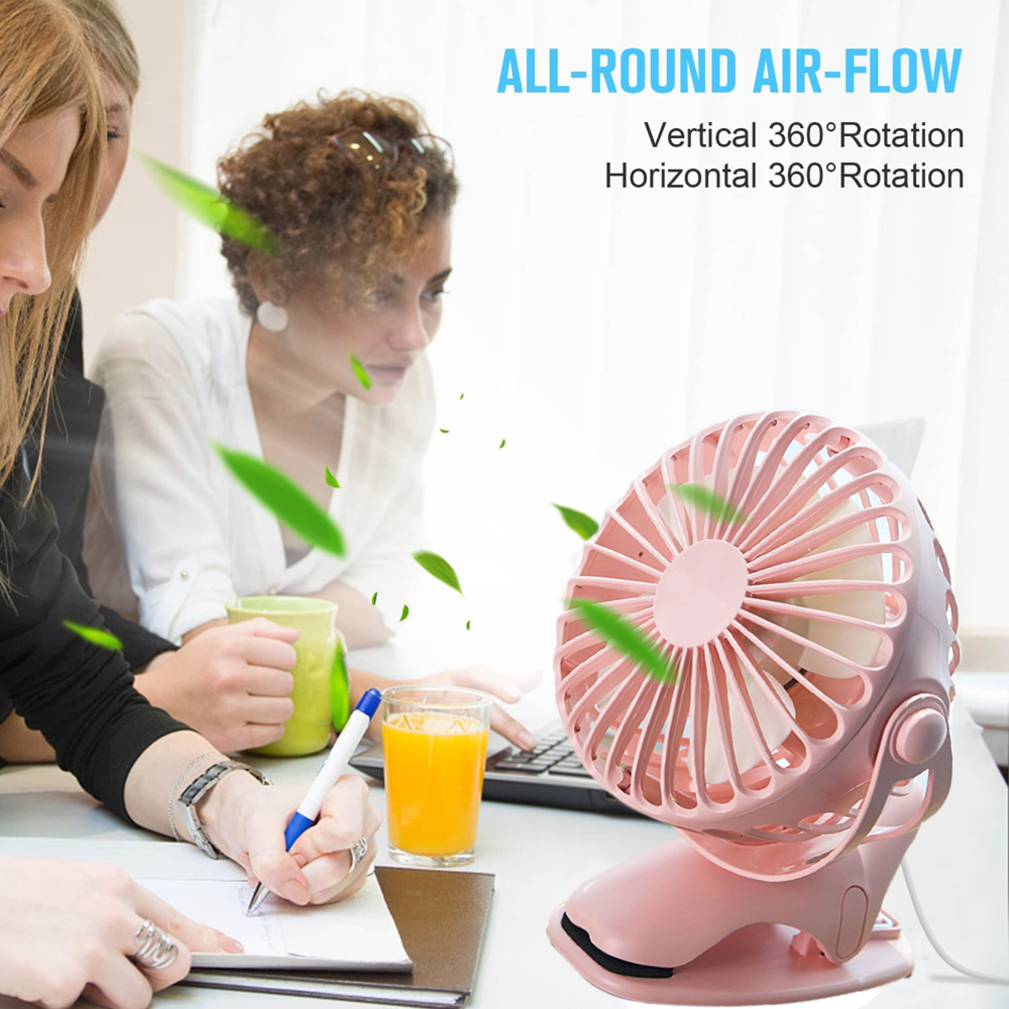 Ein kleiner rosafarbener Ventilator steht auf einem Tisch, während Personen arbeiten.