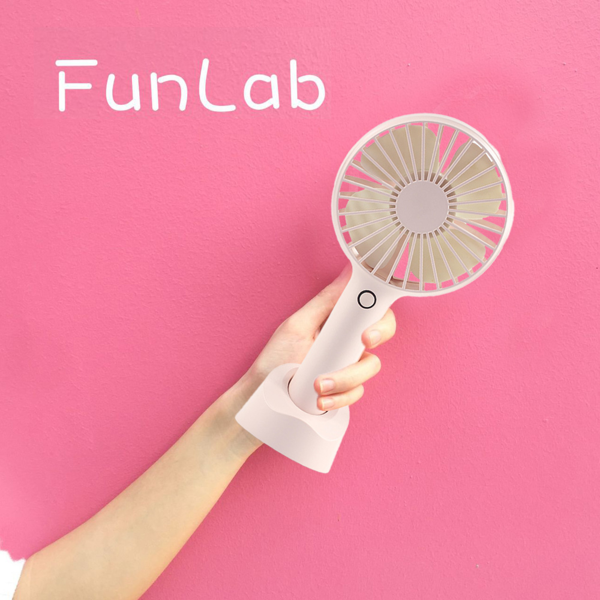 Eine Hand hält einen kleinen, weißen Ventilator vor einer rosa Wand mit der Aufschrift "FunLab".