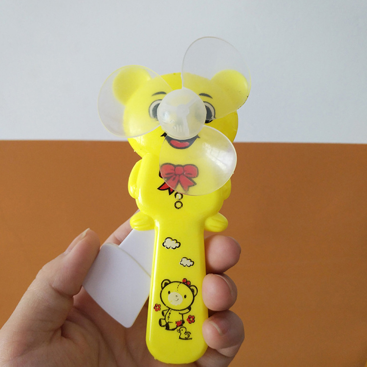 Ein gelüfterförmiger gelber Bär in einer Hand. Er hat eine rote Schleife und Cartoon-Bilder.