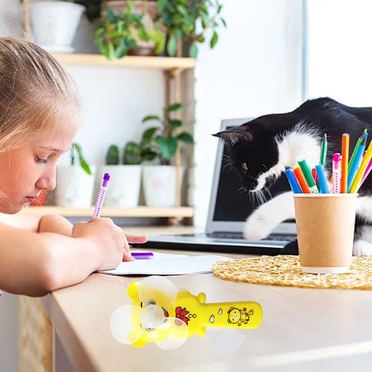 Ein Mädchen schreibt, eine Katze schaut auf einen Laptop, ein gelüfteter Lüfter liegt vorn.