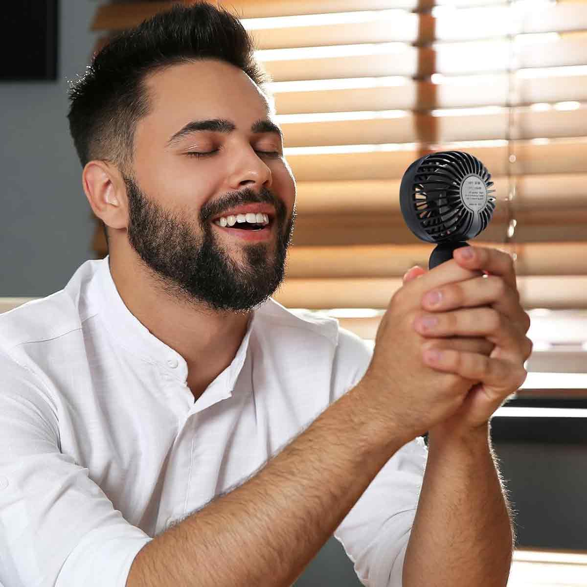 Ein Mann mit Bart im weißen Hemd hält einen kleinen schwarzen Ventilator in den Händen.