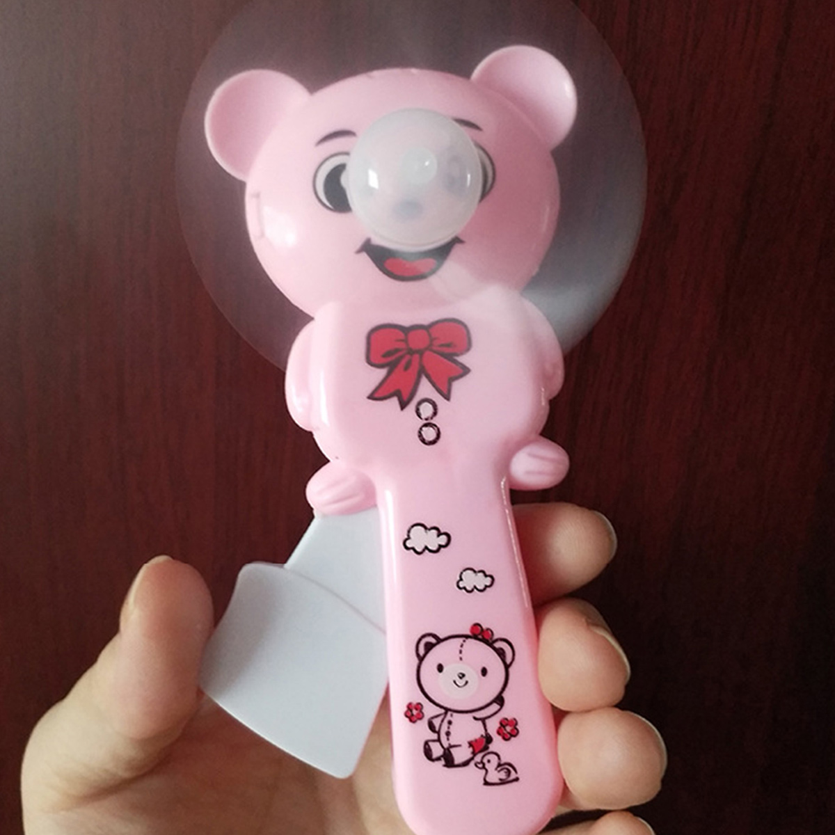 Ein pinker Ventilator in Bärenform mit roter Schleife, gehalten von einer Hand.