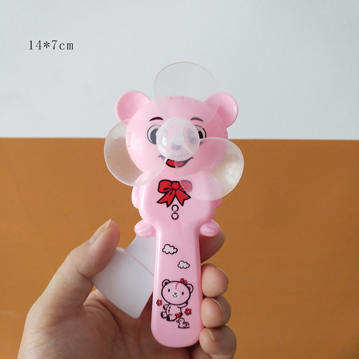 Eine Hand hält einen rosa Teddybär-Ventilator mit roten Schleifen und Wolken.