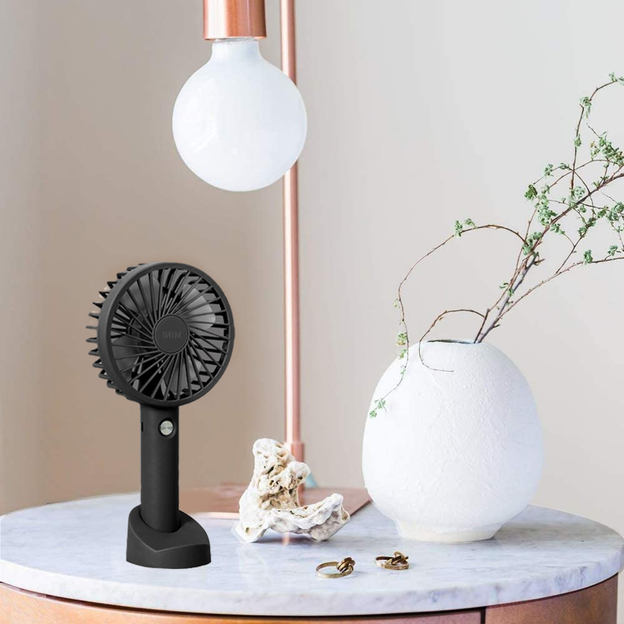 Ein schwarzer Mini-Ventilator steht auf einem Marmortisch neben einem weißen Strauß.