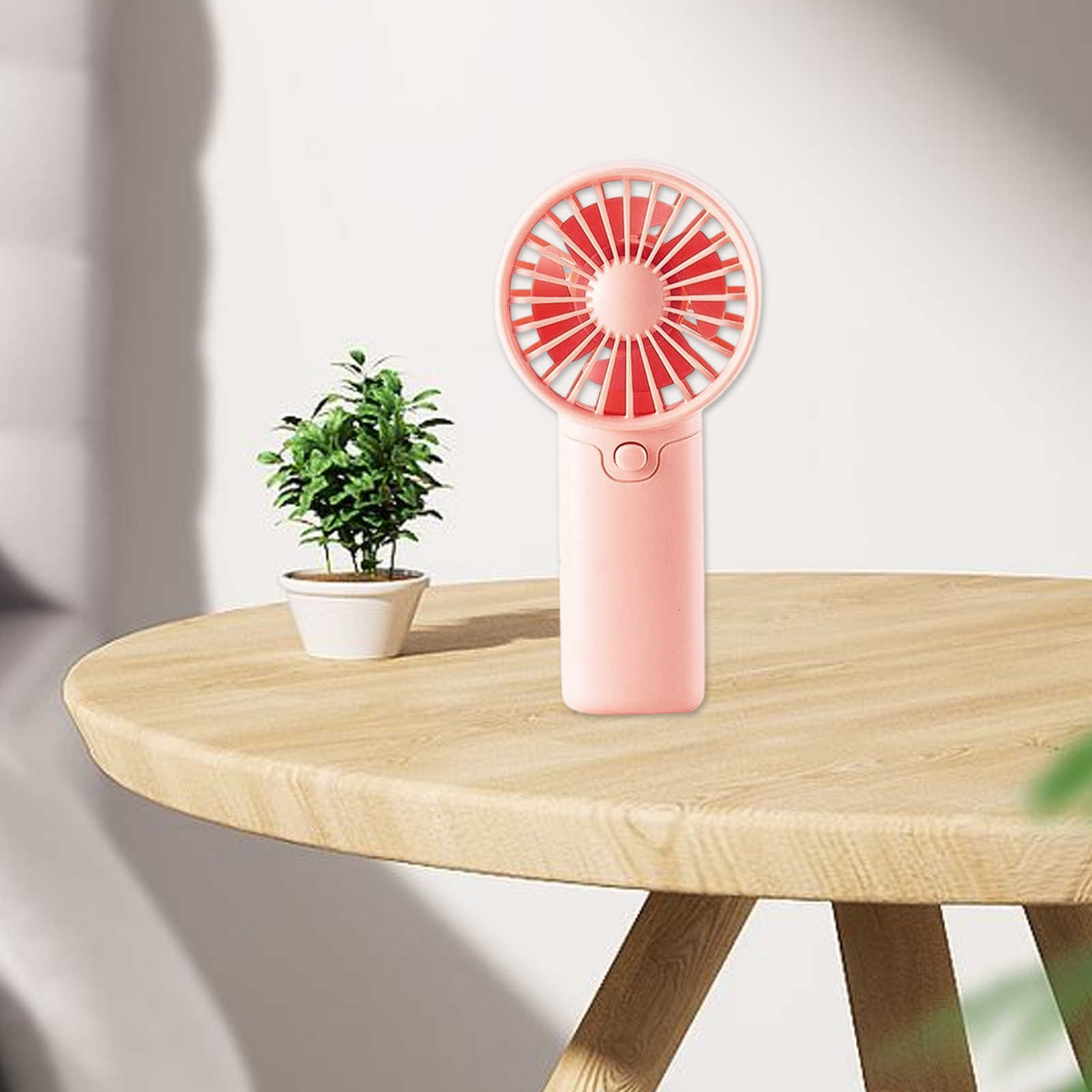 Ein rosa Handventilator mit roten Blättern steht neben einer Topfpflanze.