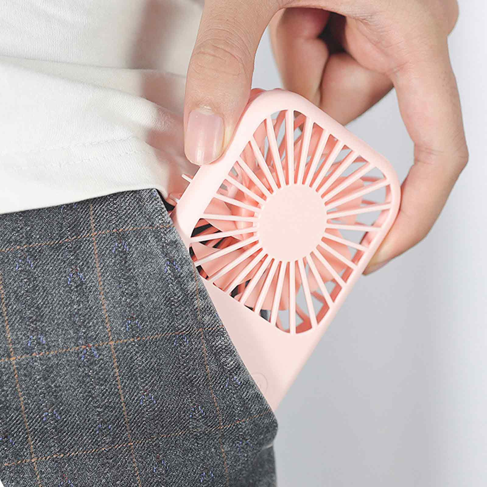 Eine Person steckt einen kleinen rosa Ventilator in die Tasche einer karierten Hose.