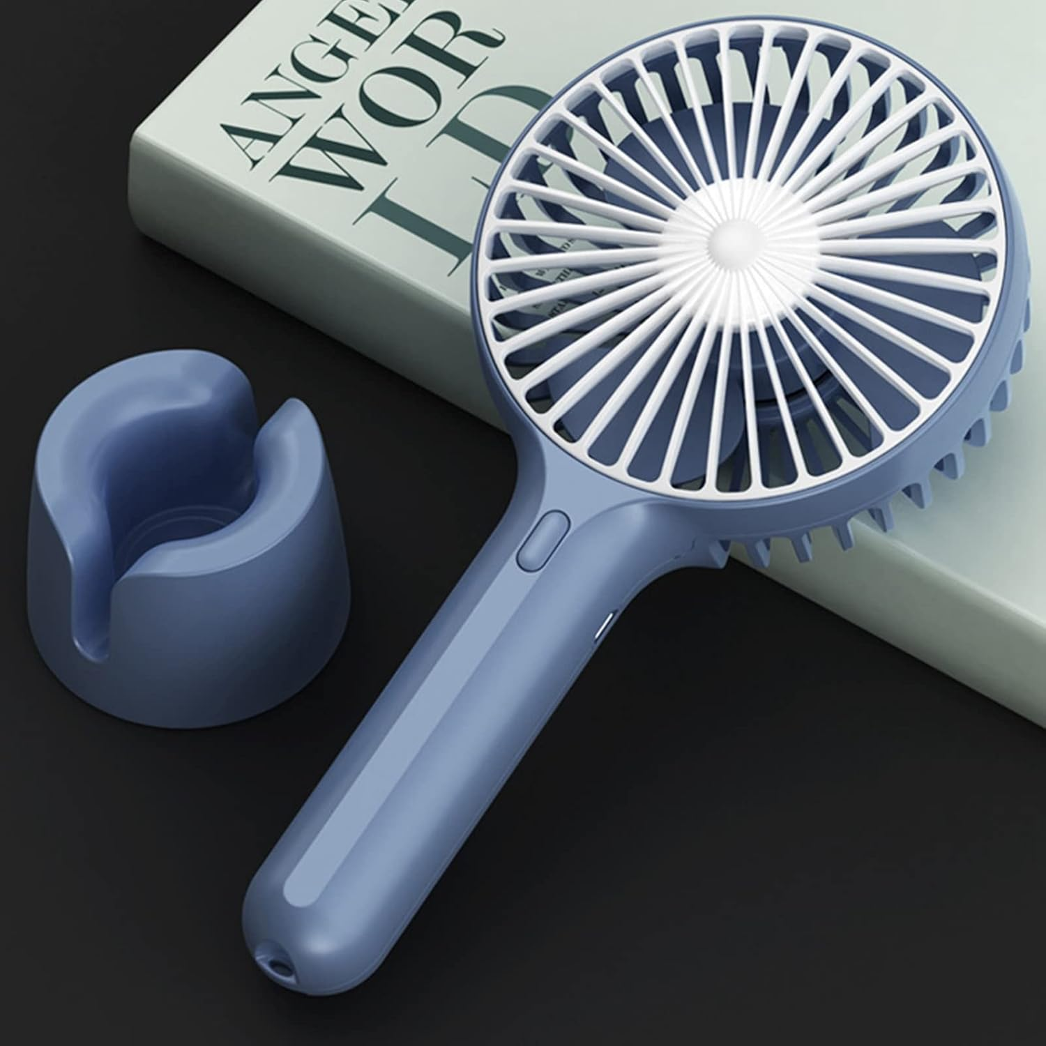 Ein blauer Handventilator mit weißem Lüftergitter und ein blauer Ständer neben einem Buch.