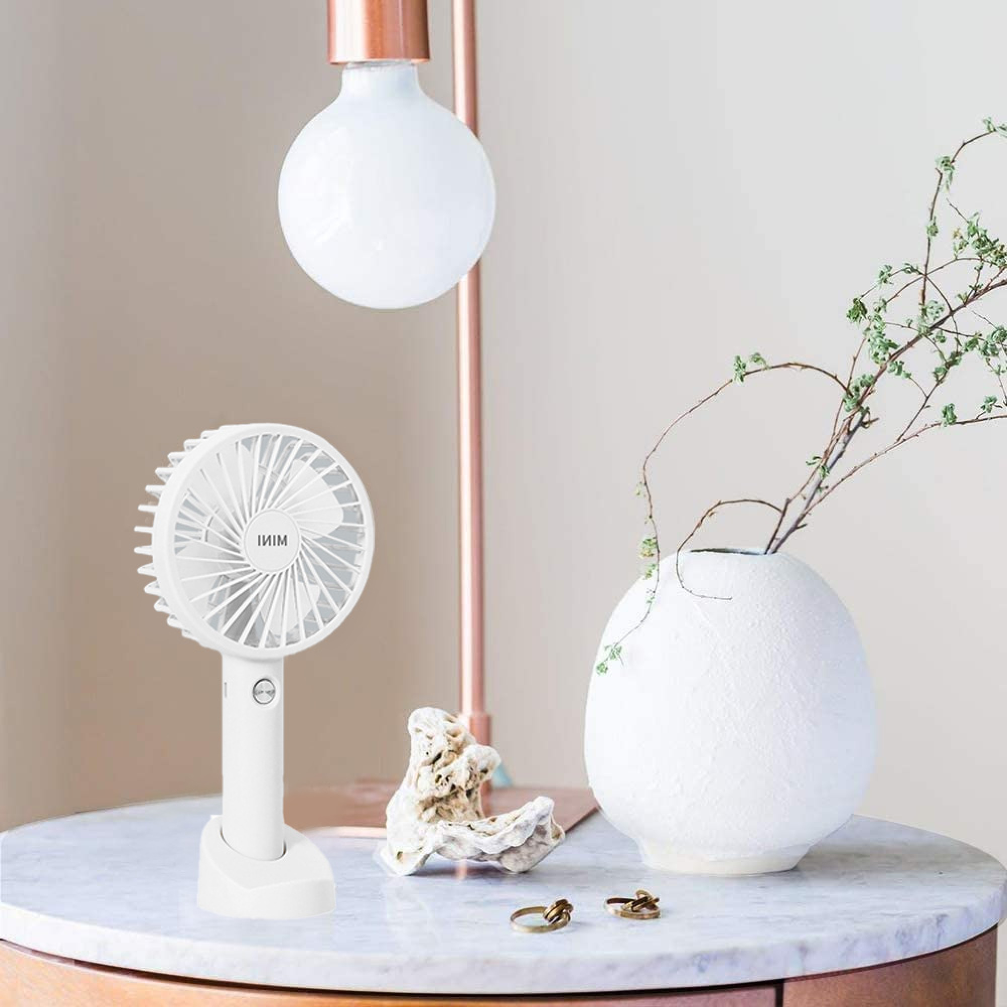 Ein weißer Mini-Ventilator steht auf einem Marmortisch neben einer Lampe und Vase.