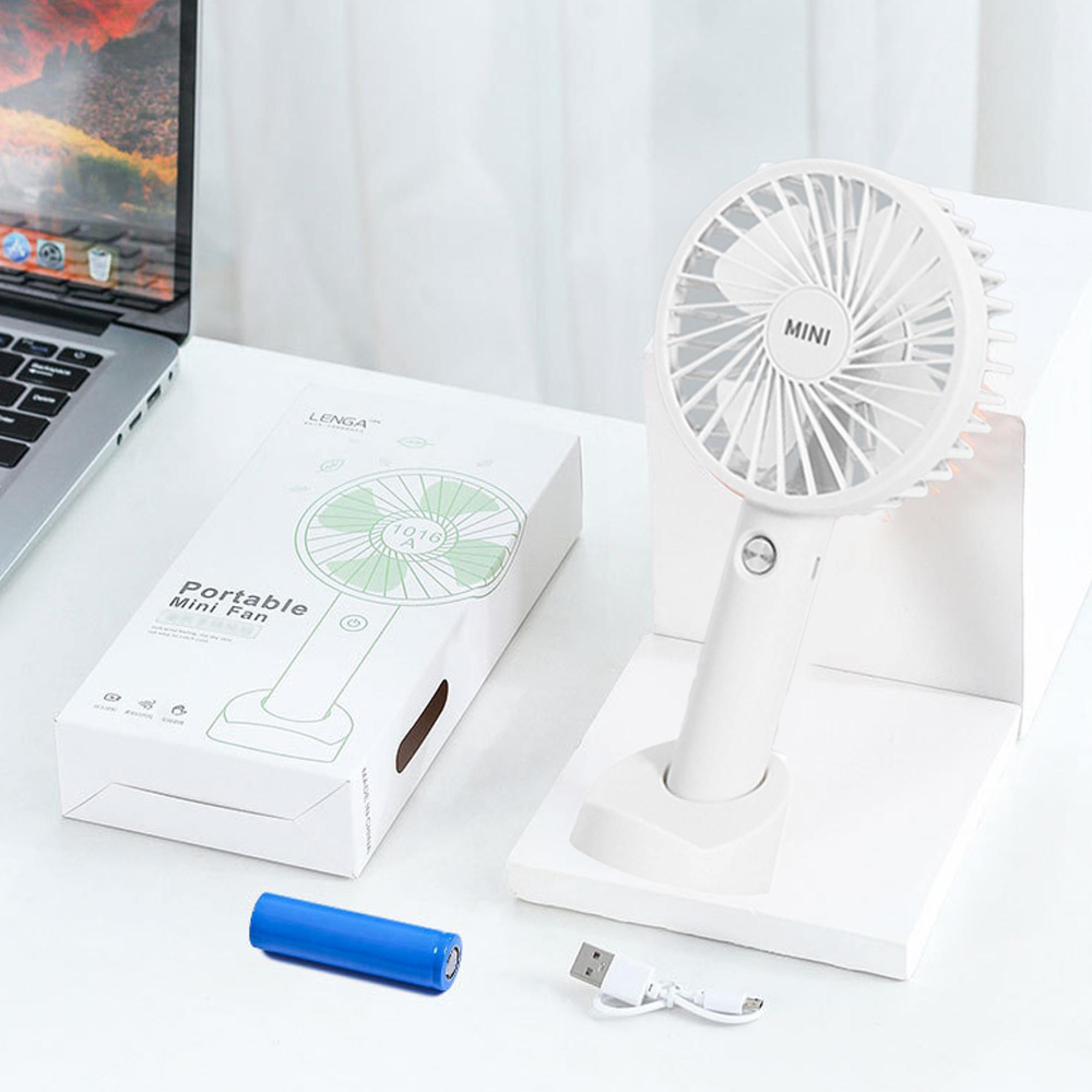 Ein weißer Mini-Ventilator steht auf einem Podest neben seiner Verpackung, einem Laptop und einer Batterie.