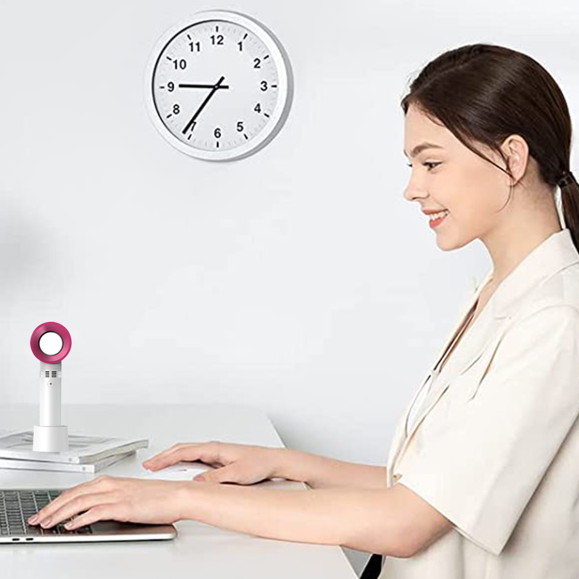 Frau am Schreibtisch mit Laptop und Lüfter, Uhr an der Wand.
