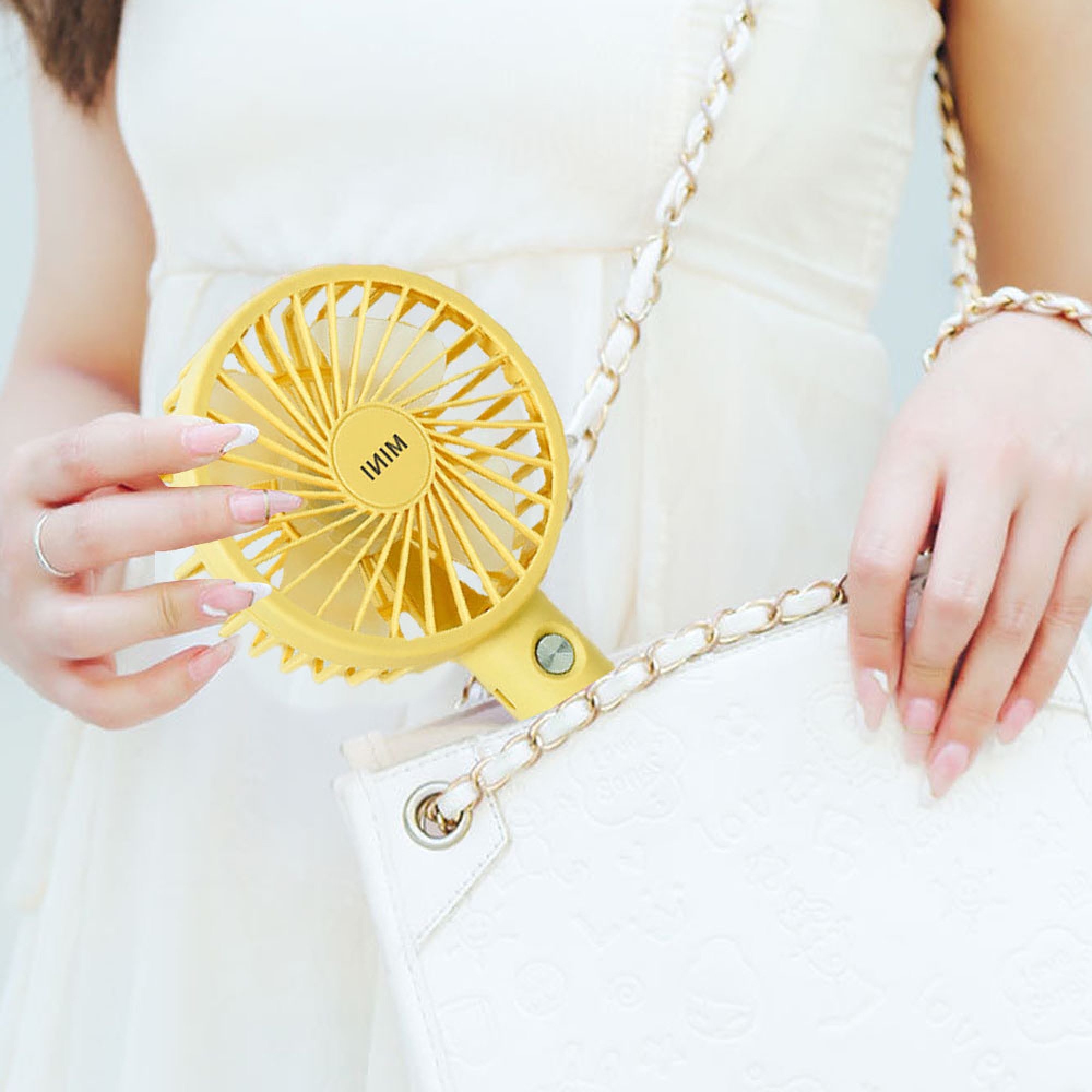Eine Person hält einen gelben Mini-Ventilator, der an einer weißen Tasche mit Kette befestigt ist.