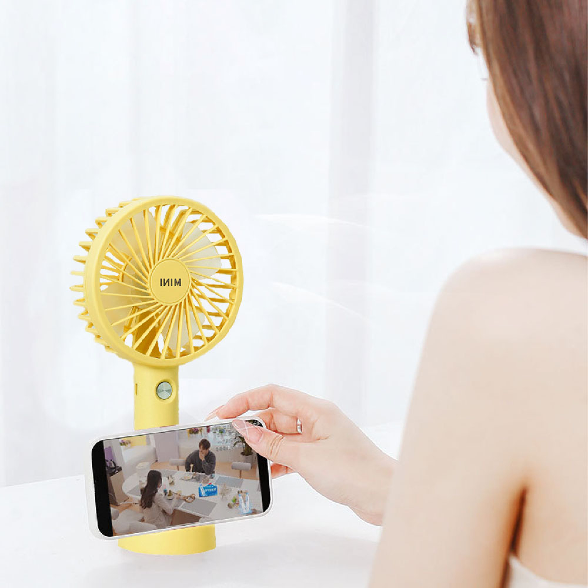 Eine Frau hält ein Handy vor einen gelben Ventilator, auf dem ein Paar zu sehen ist.