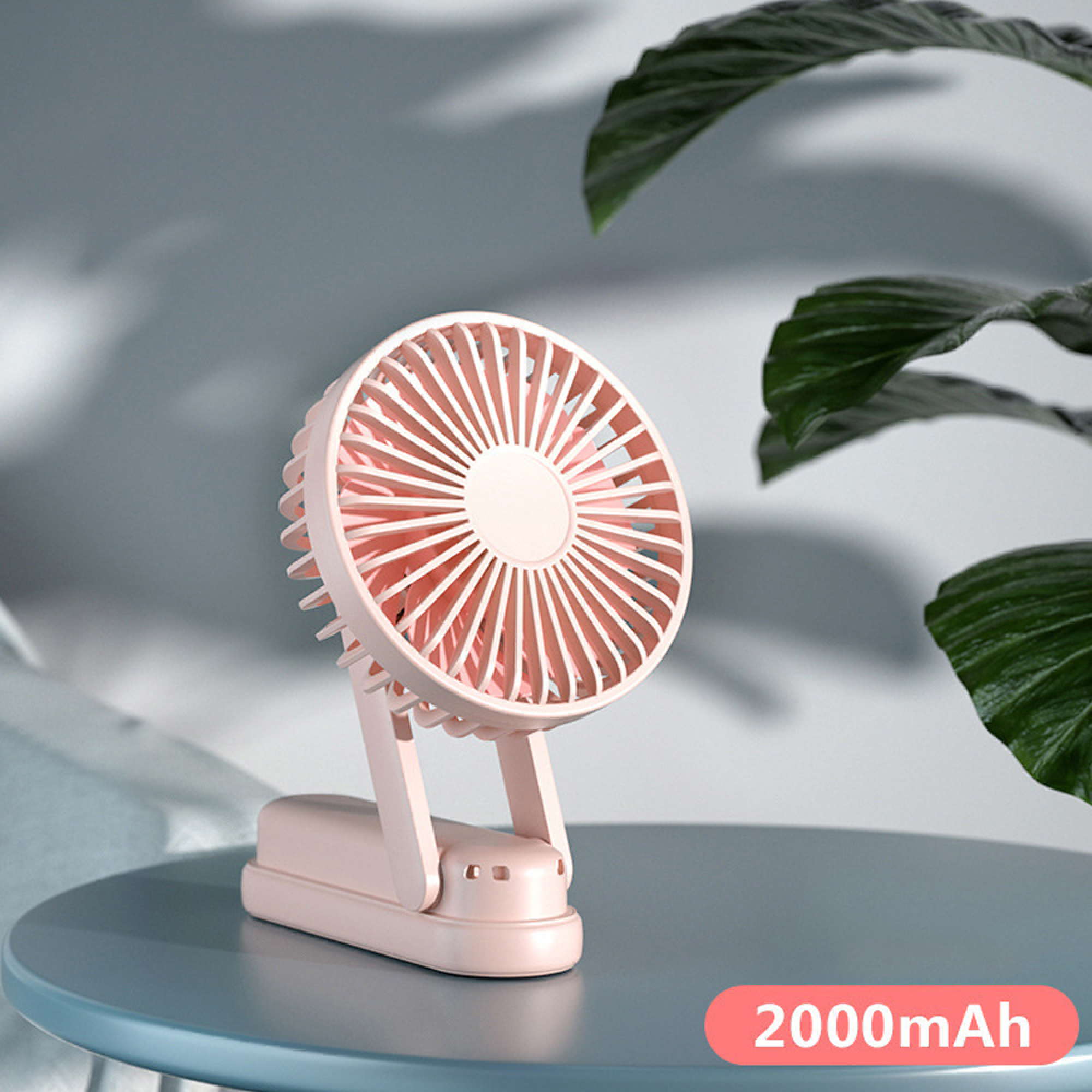 Ein kleiner, pinker Ventilator steht auf einem Tisch, daneben grüne Blätter.