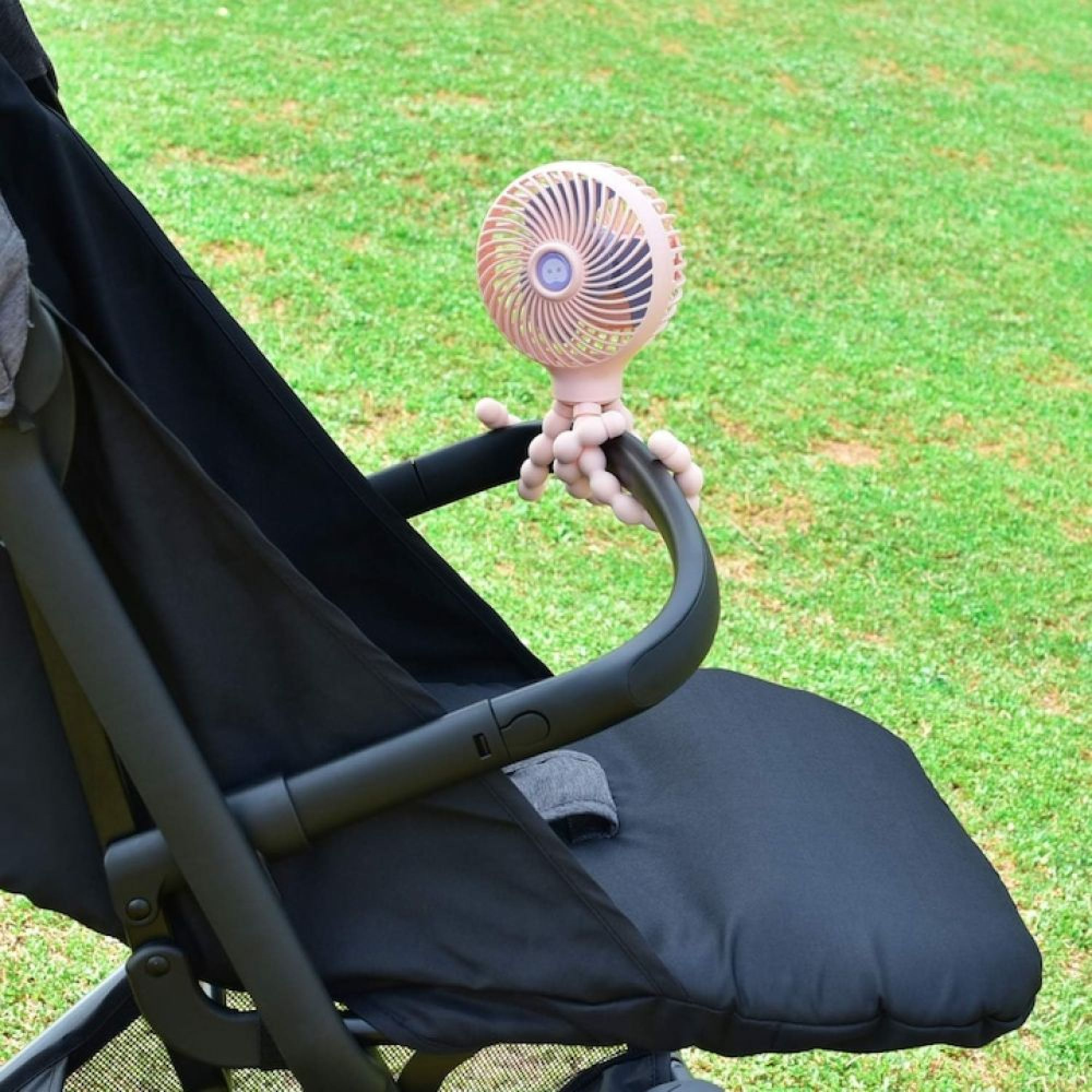 Ein rosa Ventilator mit flexiblen Beinen ist an einem Kinderwagen befestigt.