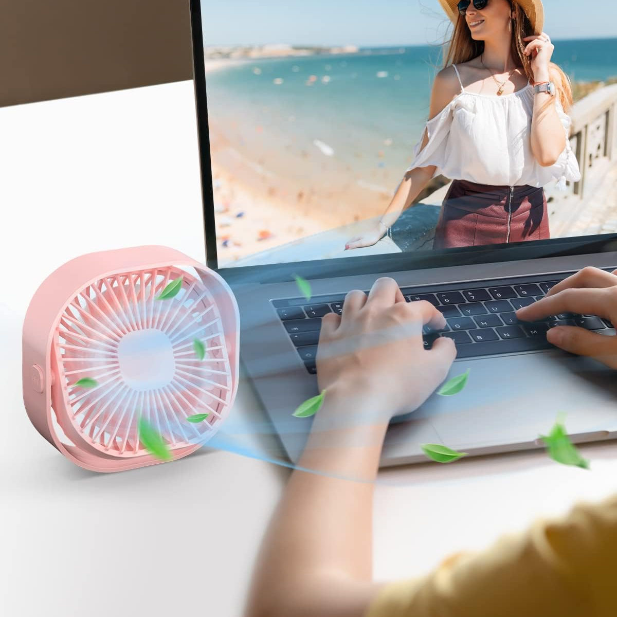 Ein rosa Ventilator kühlt eine Person, die auf einem Laptop tippt, mit Luft.