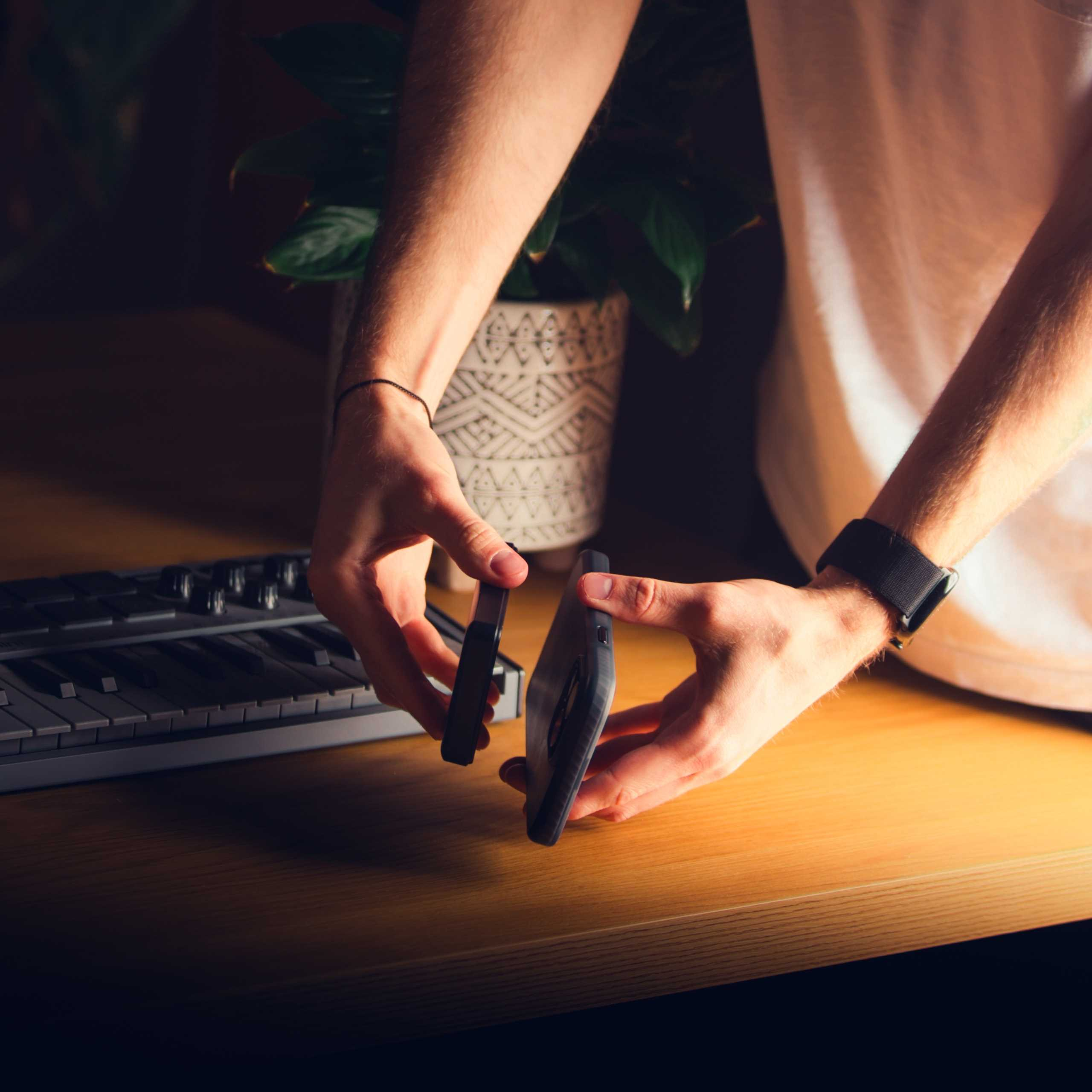 Ręce trzymają smartfon i czarny przedmiot nad klawiaturą.