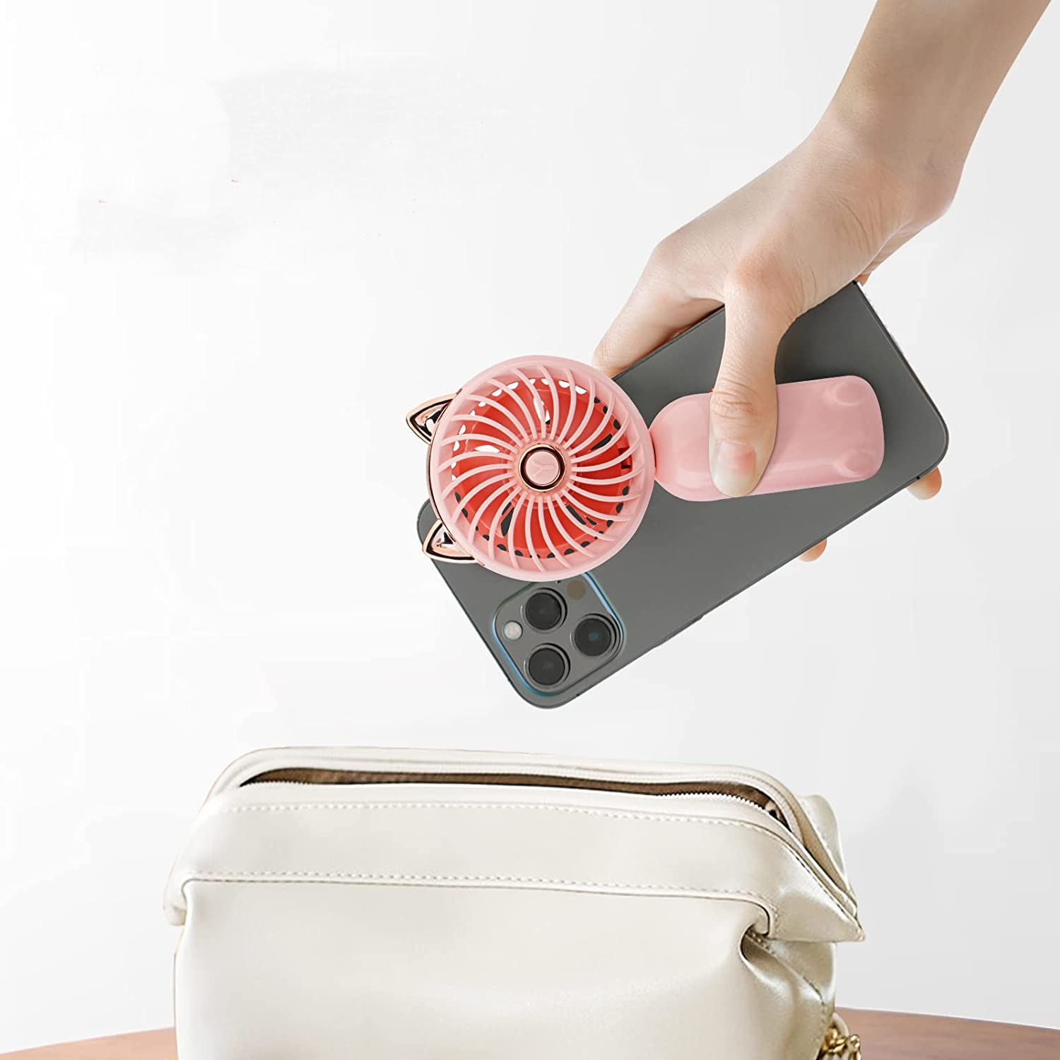 Eine Hand hält ein Handy mit angebrachtem rosa Mini-Ventilator über einer offenen weißen Tasche.