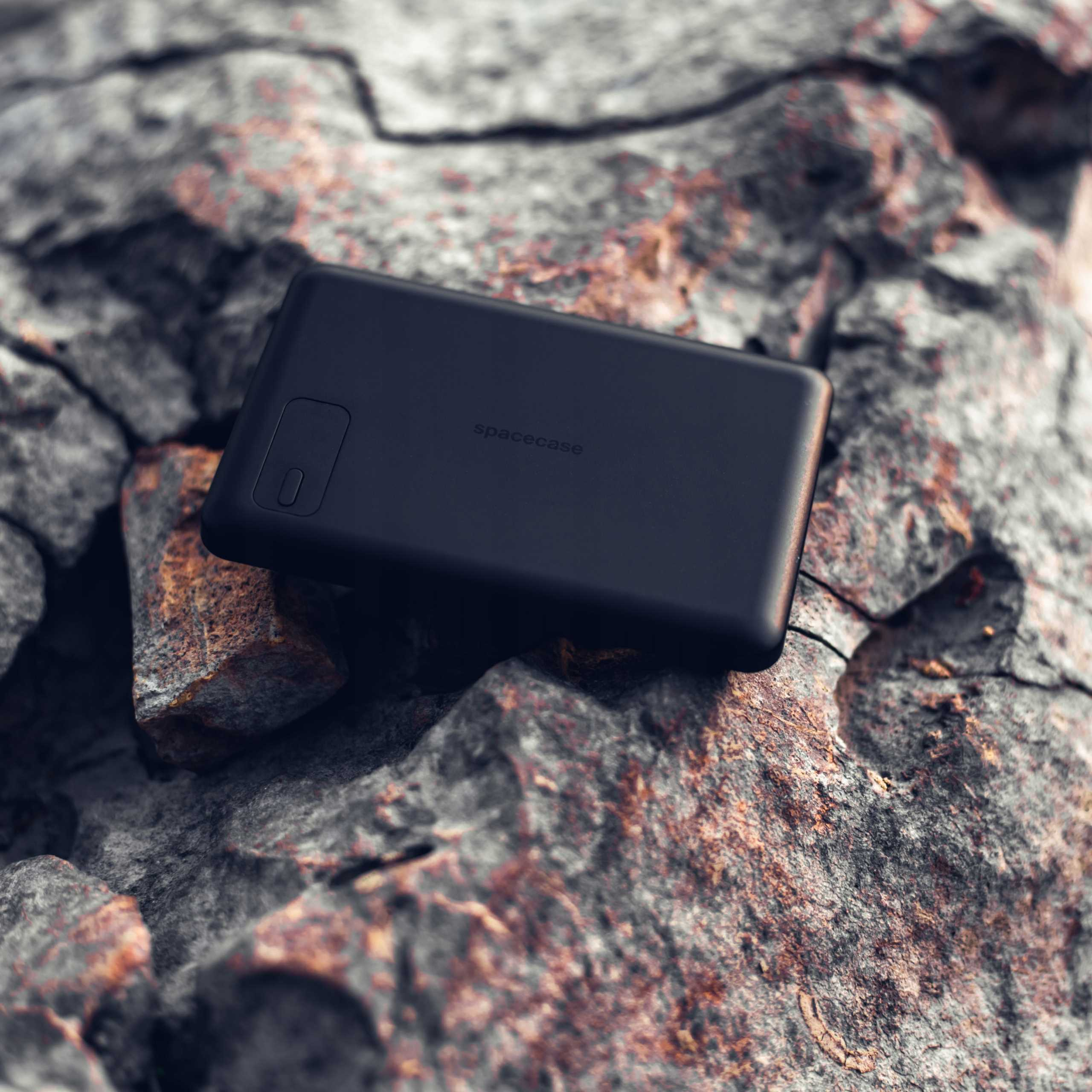 Czarna powerbanka spacecase leży na surowych skałach.
