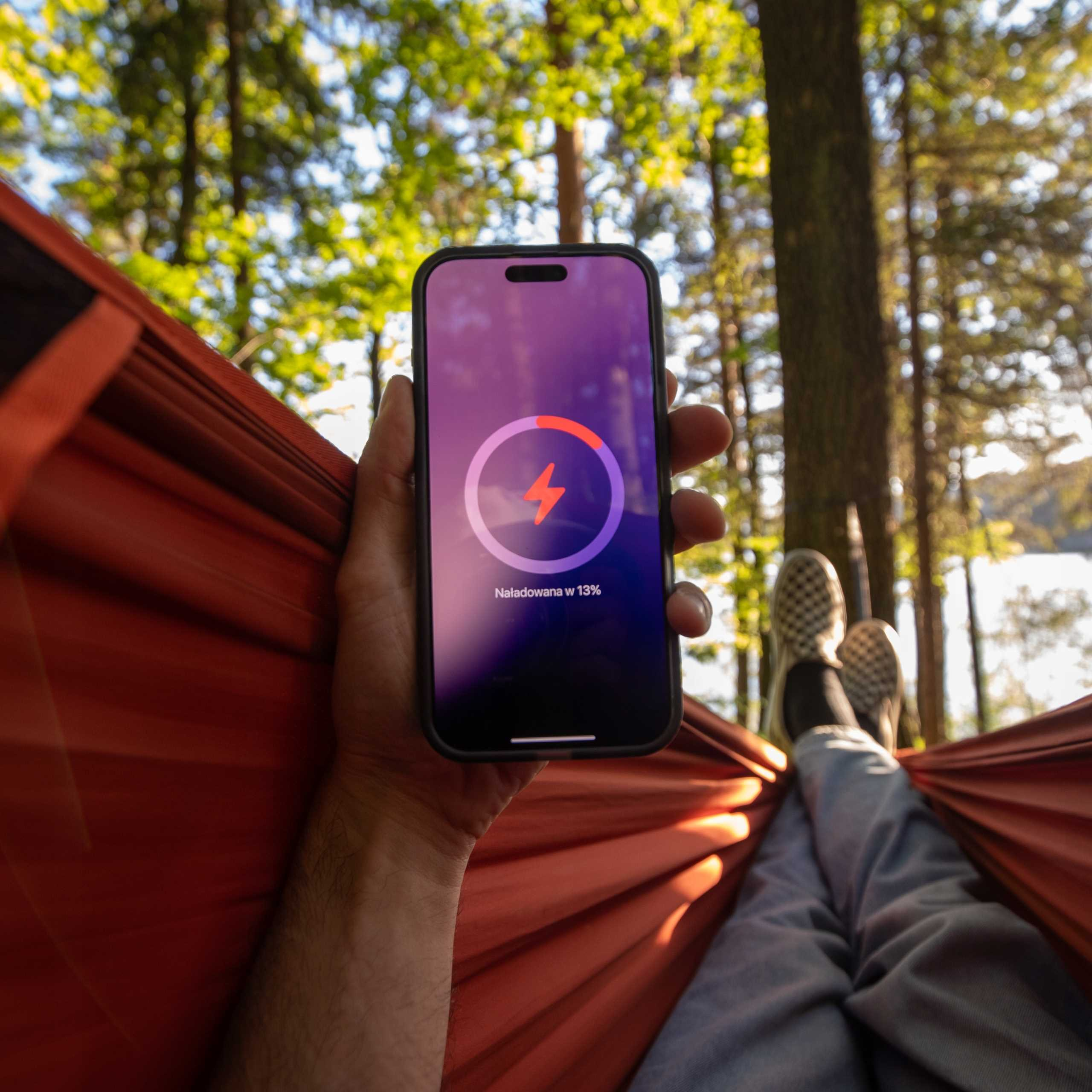 Osoba w hamaku trzyma telefon z 13% baterii.