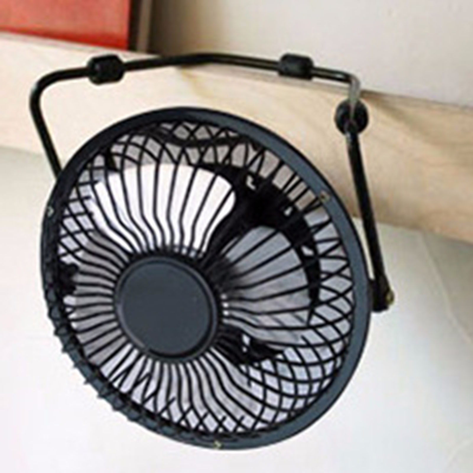 Ein kleiner schwarzer Ventilator mit Metallgitter hängt an einem Holzbrett.