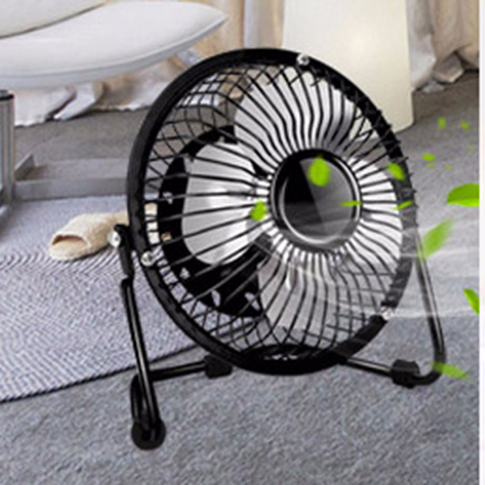 Ein schwarzer Schreibtischventilator mit Metallgitter steht auf einem grauen Teppich, neben einem Hausschuh.