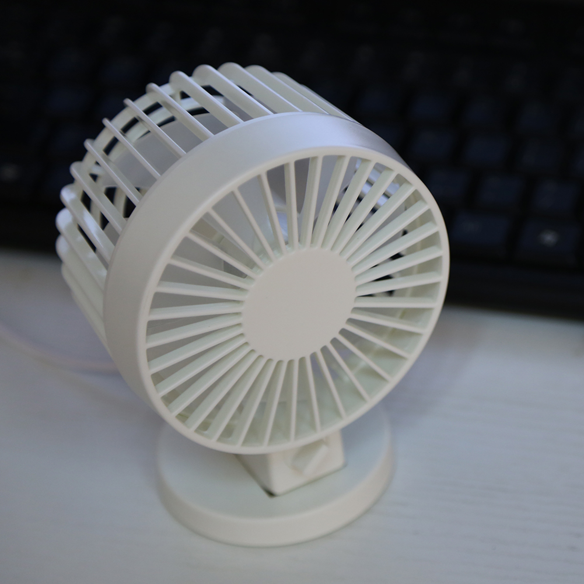 Ein kleiner, weißer Tischventilator steht auf einer hellen Oberfläche, mit einer Tastatur im Hintergrund.