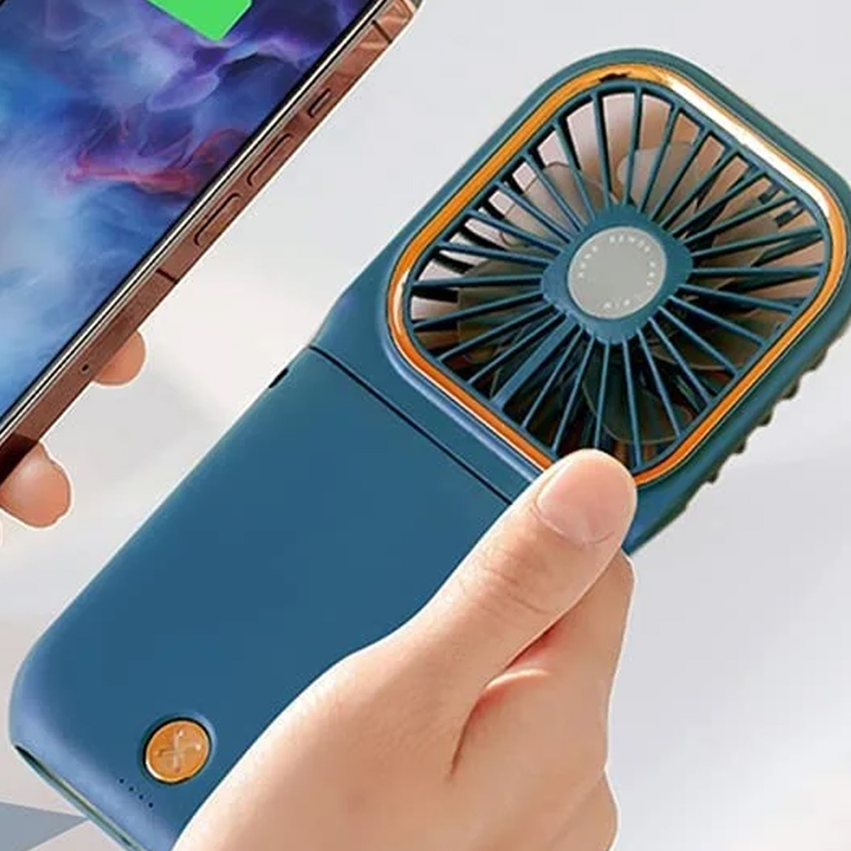 Eine Hand hält einen blauen tragbaren Ventilator neben einem Smartphone mit buntem Hintergrundbild.